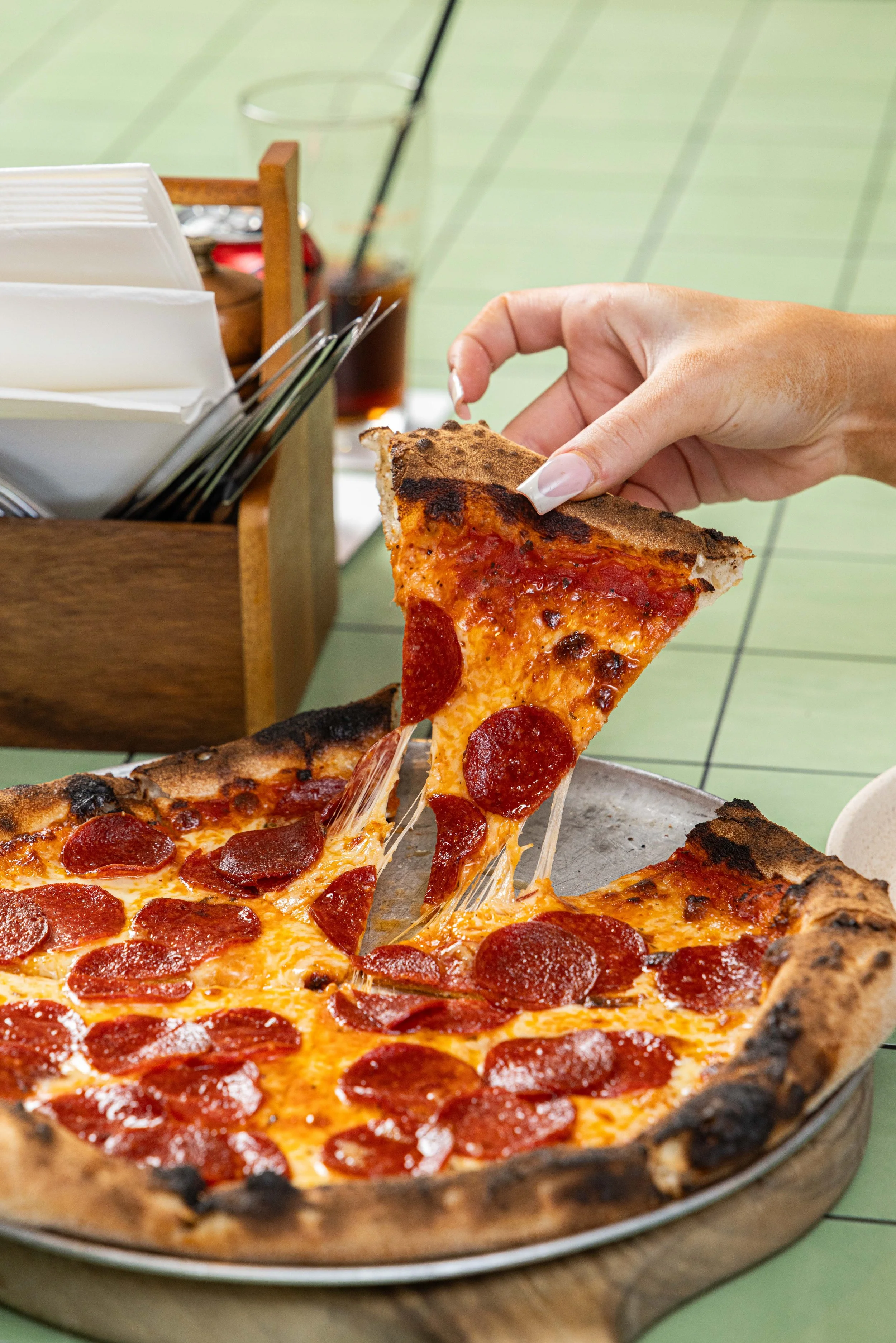 A cheesy pepperoni pizza on a green tiled table.