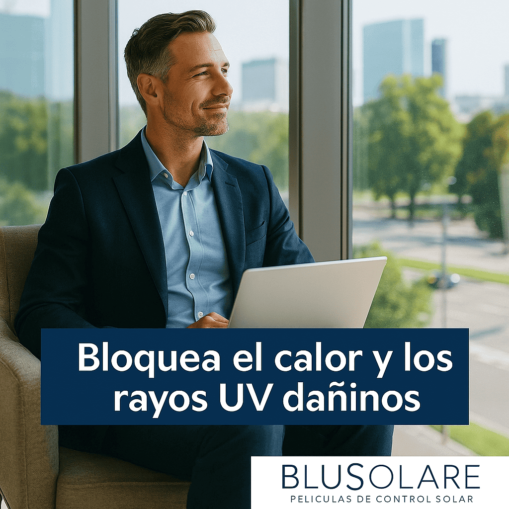 Hombre con barba y cabello gris sentado junto a ventana con vista a árboles y edificios, usando traje azul y sosteniendo una laptop.