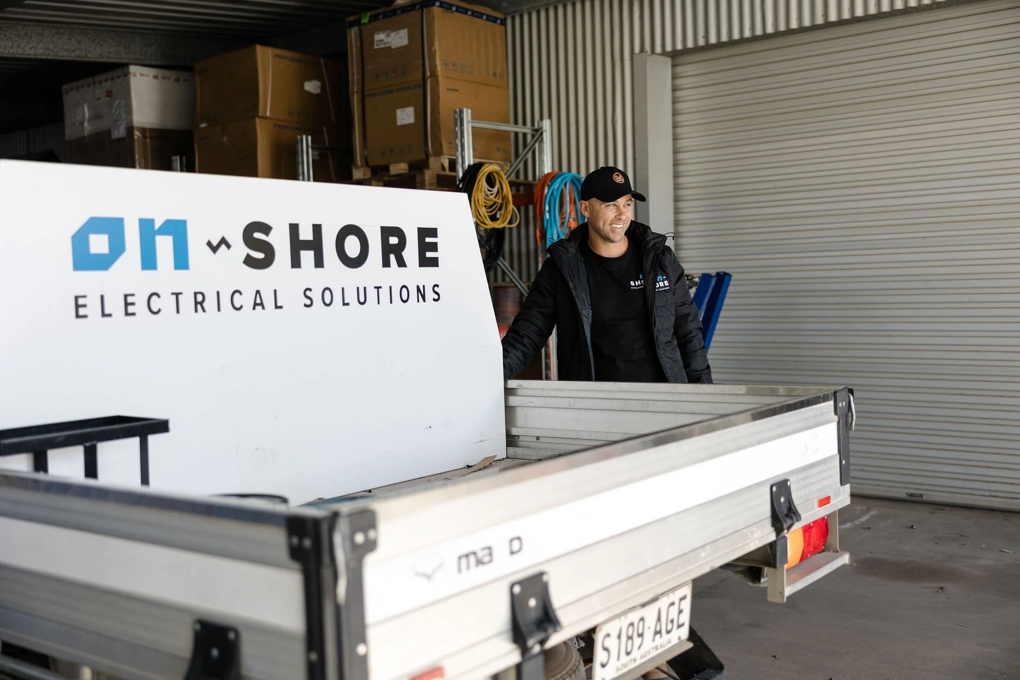 Electrician standing behind a truck displaying an Onshore Electrical Solutions sign at a warehouse loading area