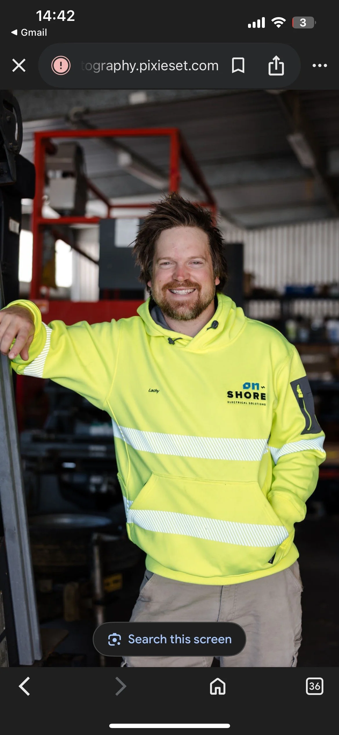 Smiling man in a neon yellow Shore Electrical Solutions hoodie standing inside an industrial workshop