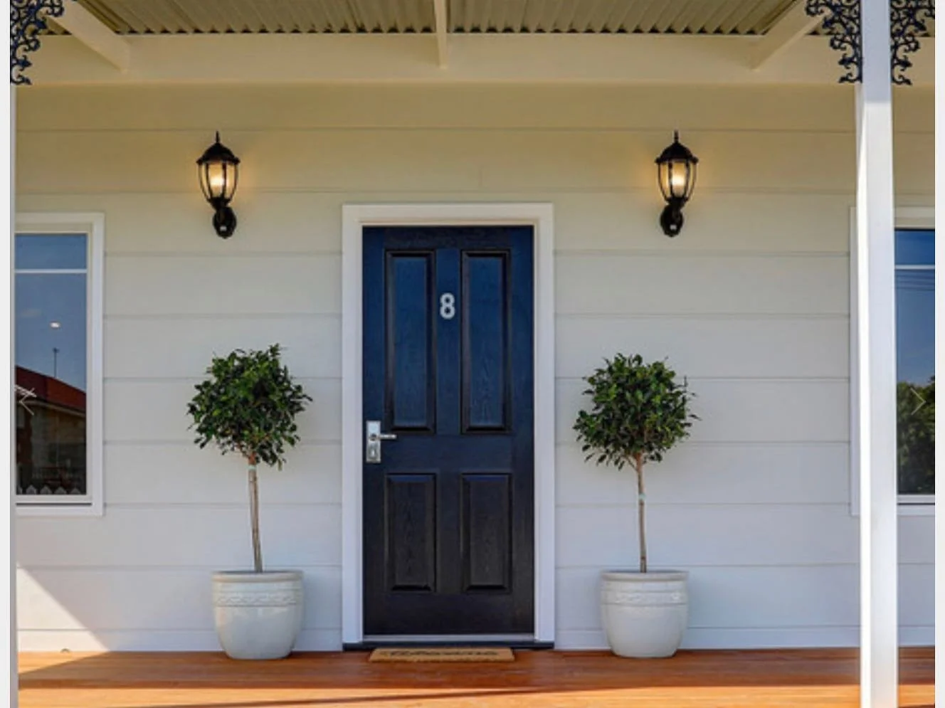 Front porch with a dark blue door numbered 8, two potted topiary trees, and wall lanterns.
