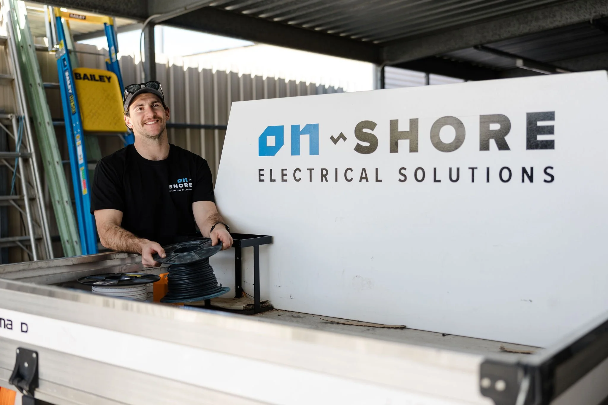 Electrician holding a spool of cable beside an Onshore Electrical Solutions sign in a work truck