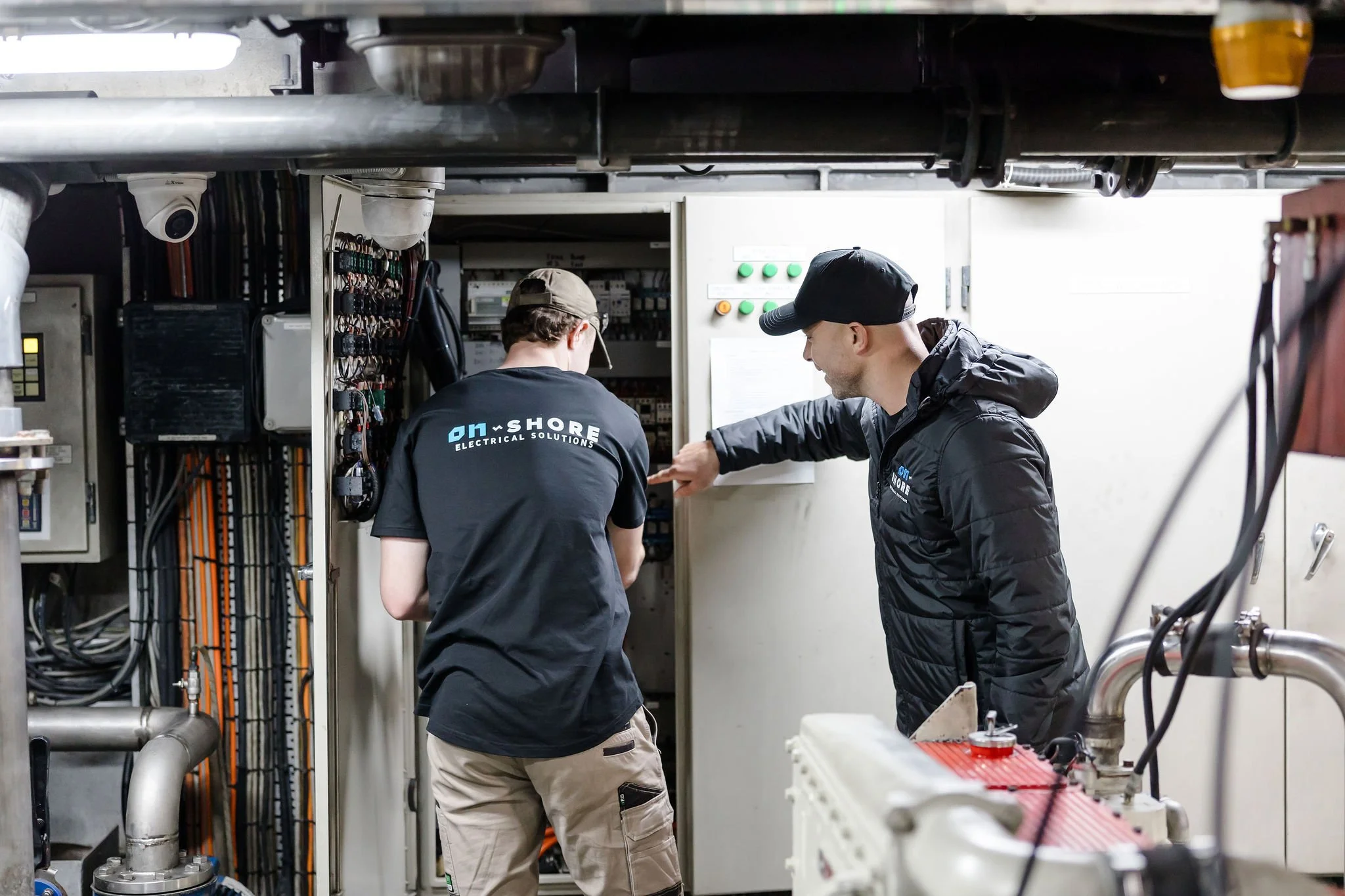 Two electrical technicians inspecting industrial control panels and machinery in a utility room