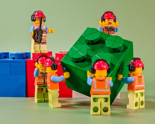 Three kids sitting on the floor, drawing and coloring on a large sheet of paper with markers, surrounded by art supplies, in a room with a brick wall background.