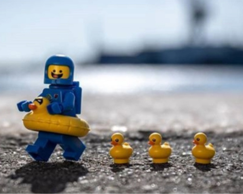 Two women playing soccer outdoors on a grassy field with trees and cloudy sky in the background.