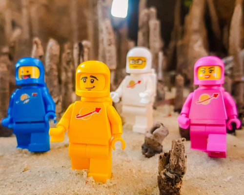 Two men sitting on the grass outdoors having a conversation, with one man in a wheelchair nearby, surrounded by trees and white flowers.