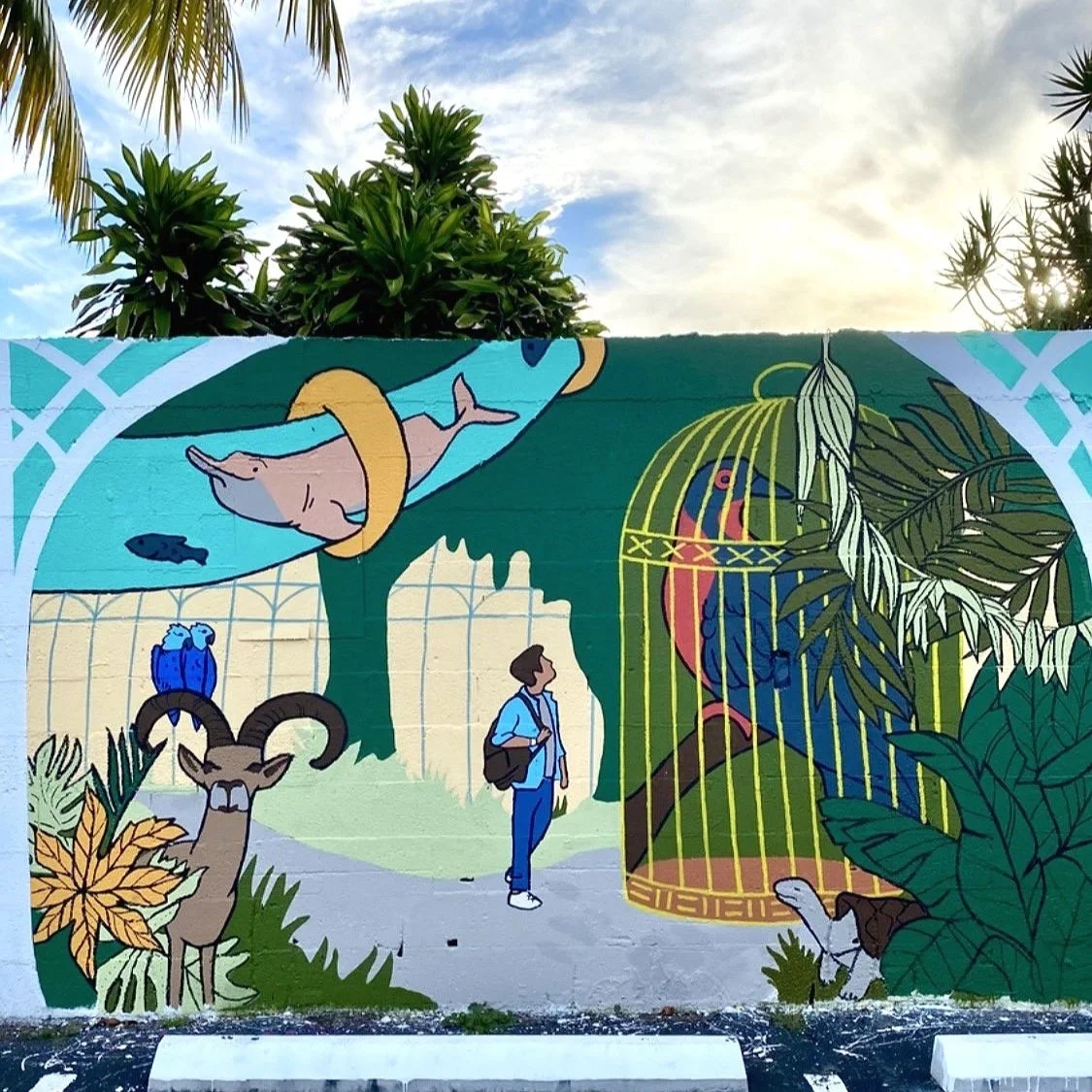 Colorful mural depicting various animals including a whale, a bird in a cage, a ram with large horns, and a small animal near plants, with a person looking at the artwork in an outdoor setting.