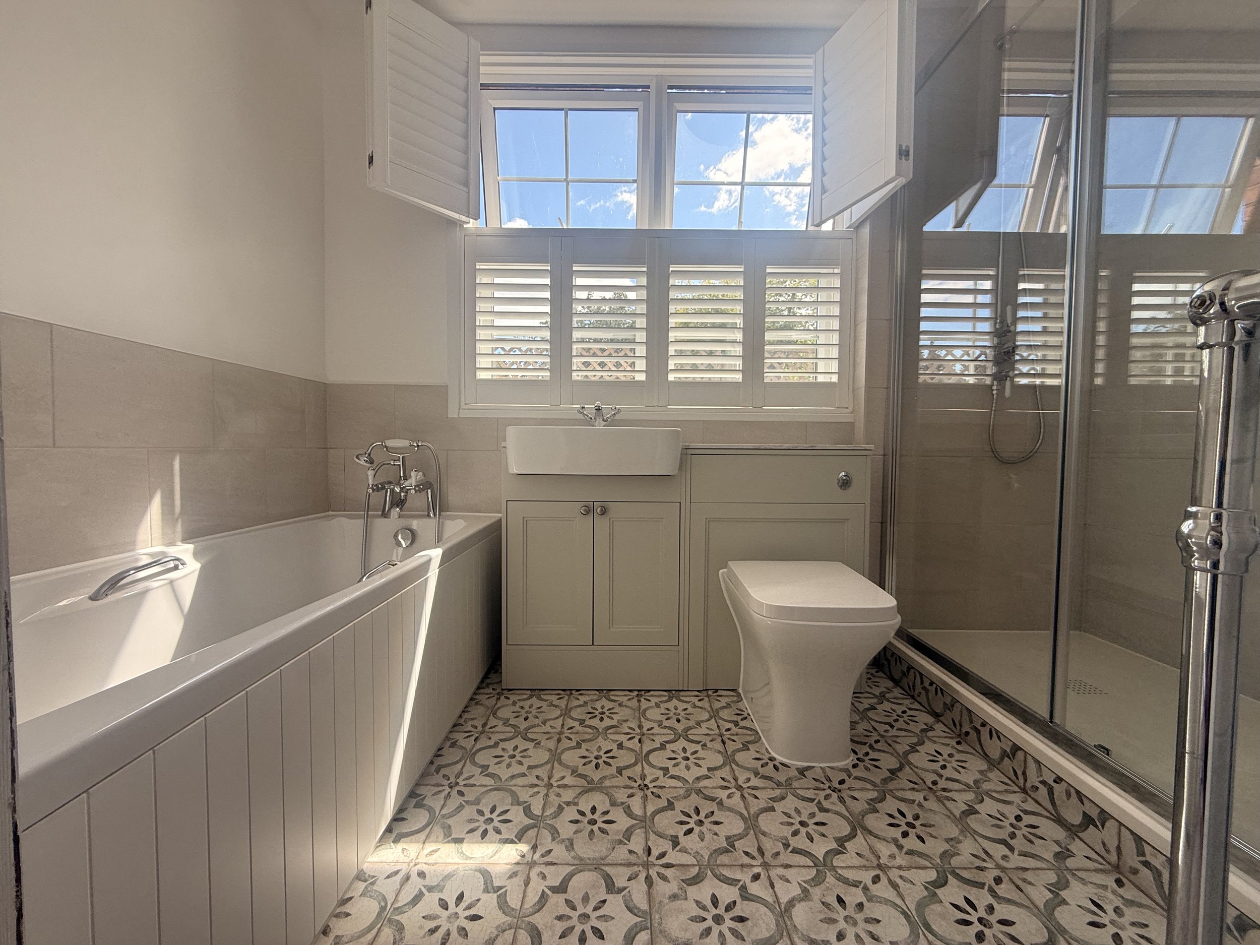 Bathroom with a bath, separate shower enclosure, fitted basin furniture and patterned floor tiles.