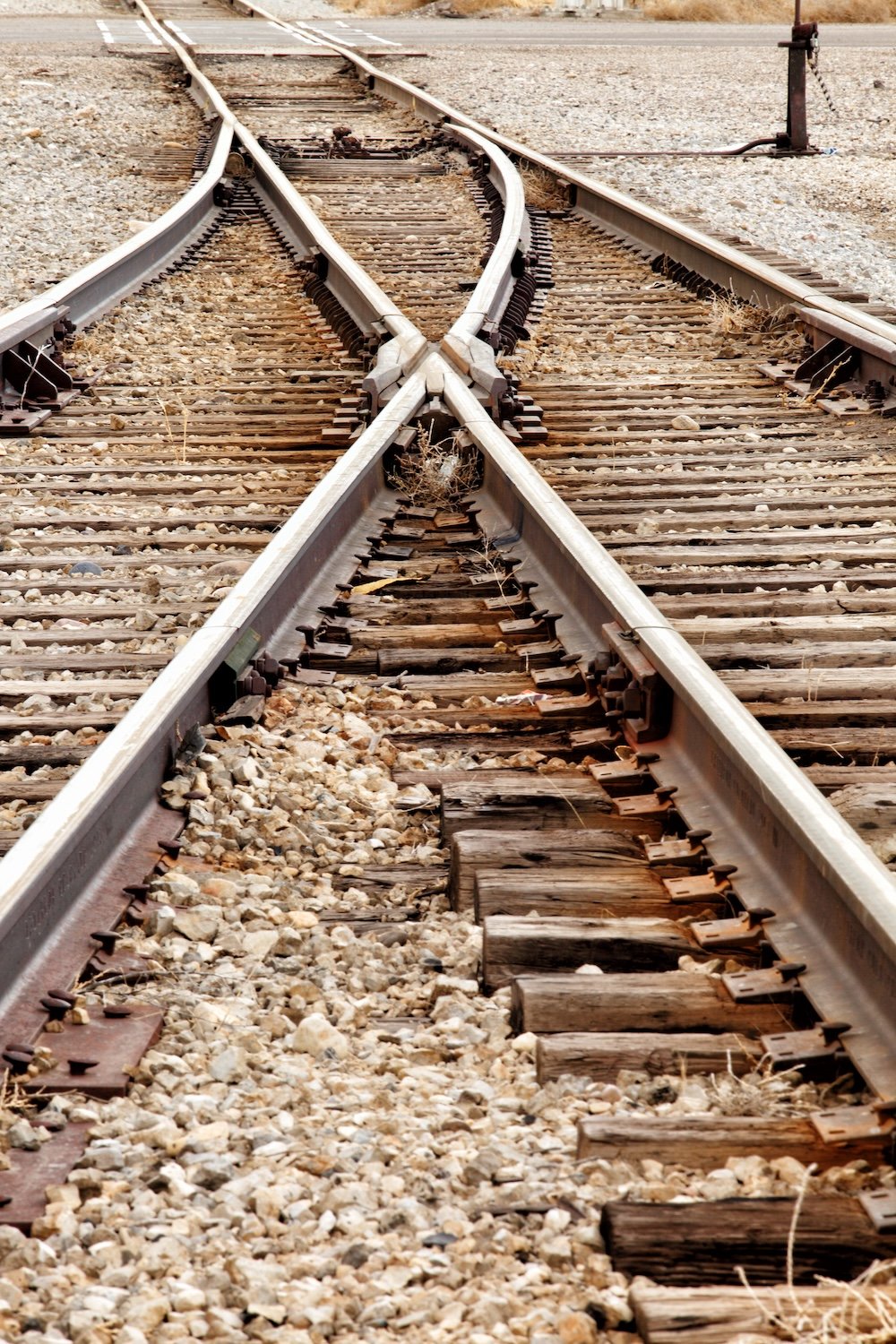 Multiple railway tracks crossing each other on a gravelly ground in a desert-like area.