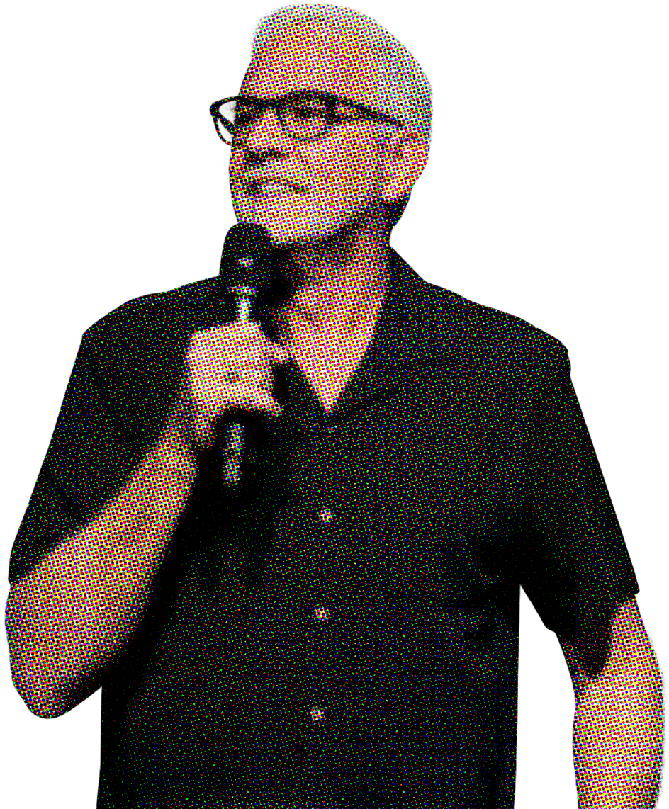 Person with glasses and bald head speaking into a microphone on a black background.