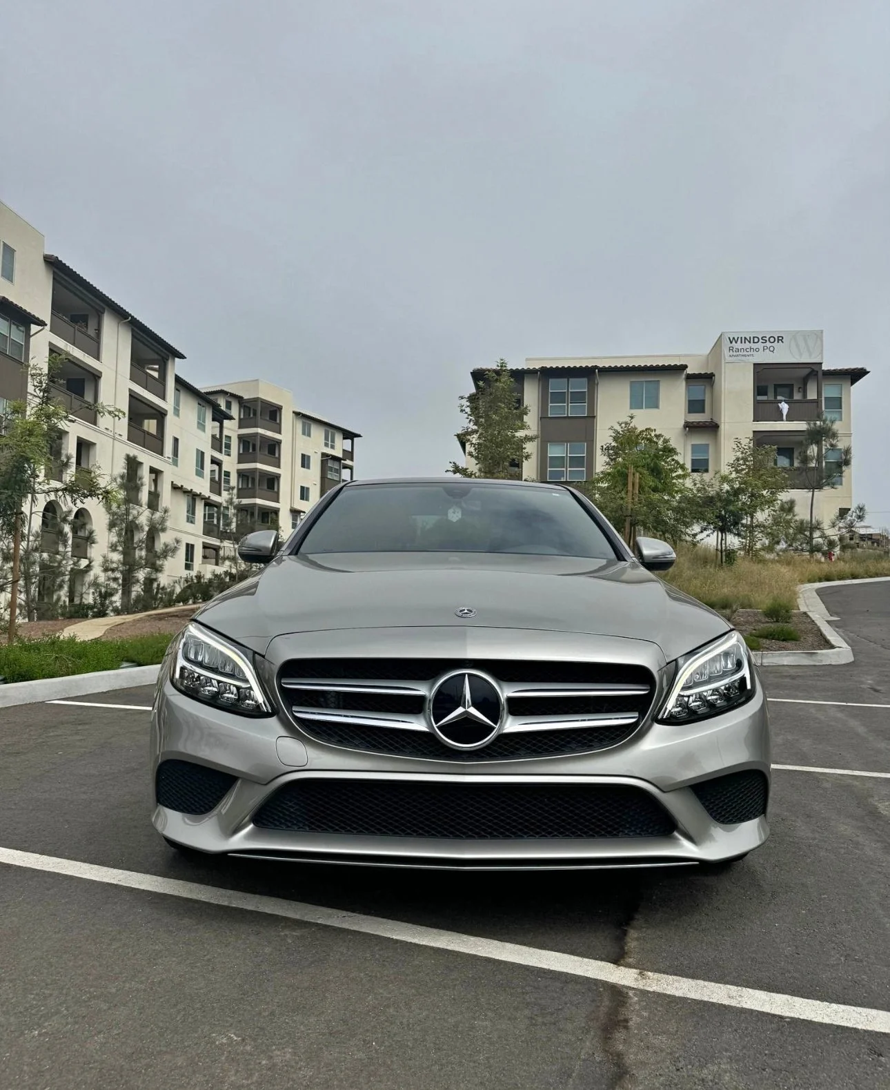 Silver Mercedes-Benz car parked in an outdoor parking lot with residential buildings in the background.