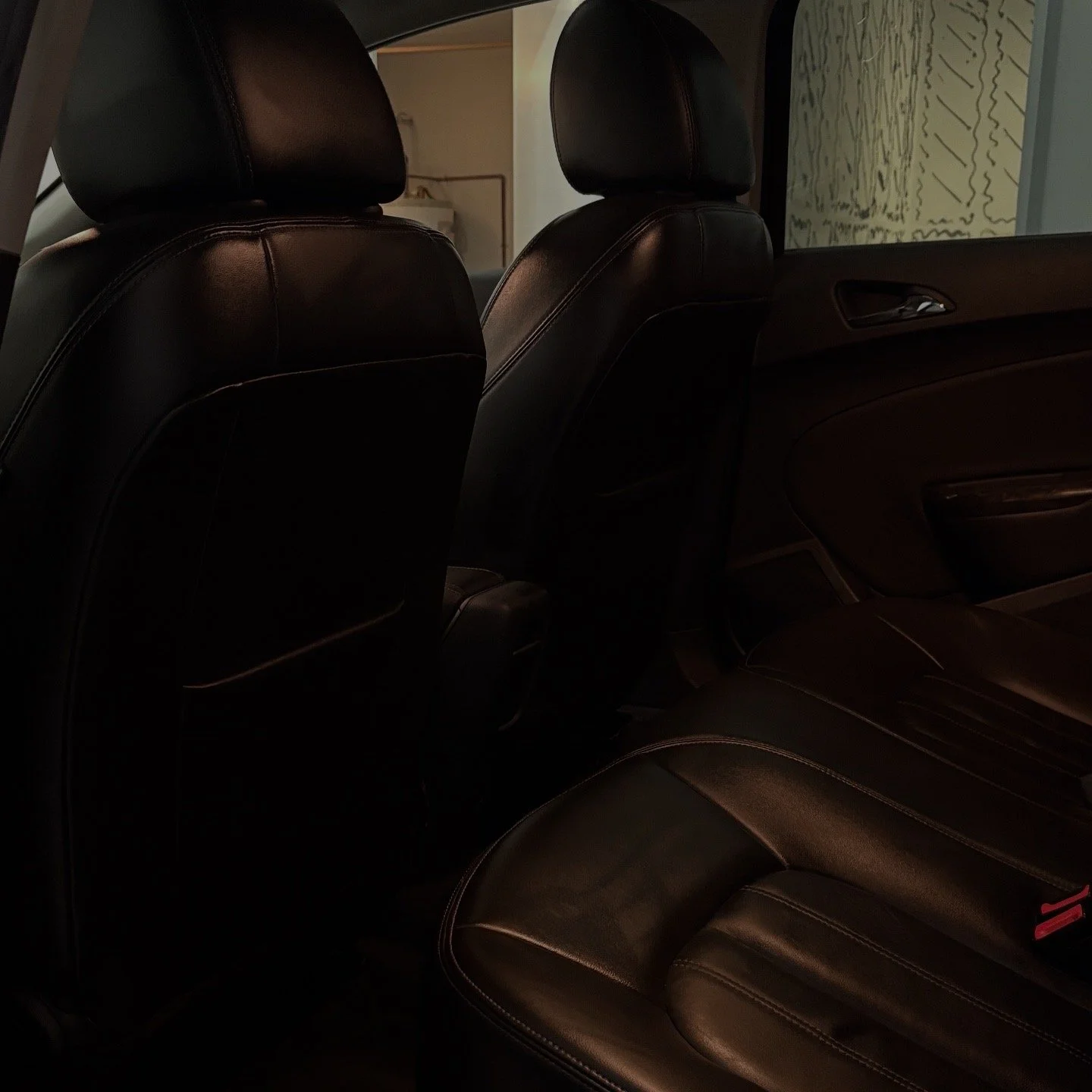 Backseat area of a car with black leather seats, headrests, and door panel visible in a dimly lit setting.