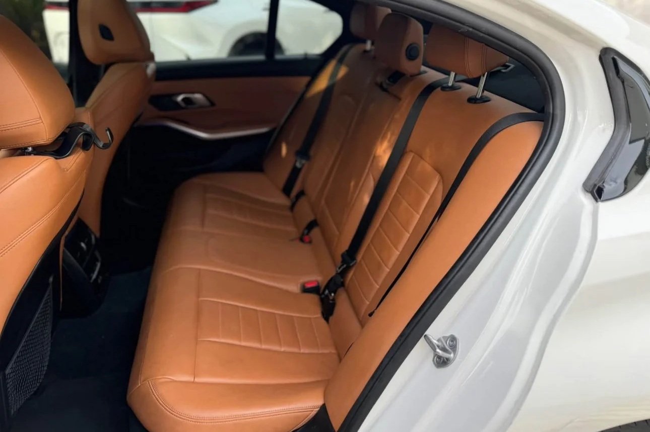 The interior of a white SUV showing tan leather back seats with black seat belts and tan upholstery on the door panels.