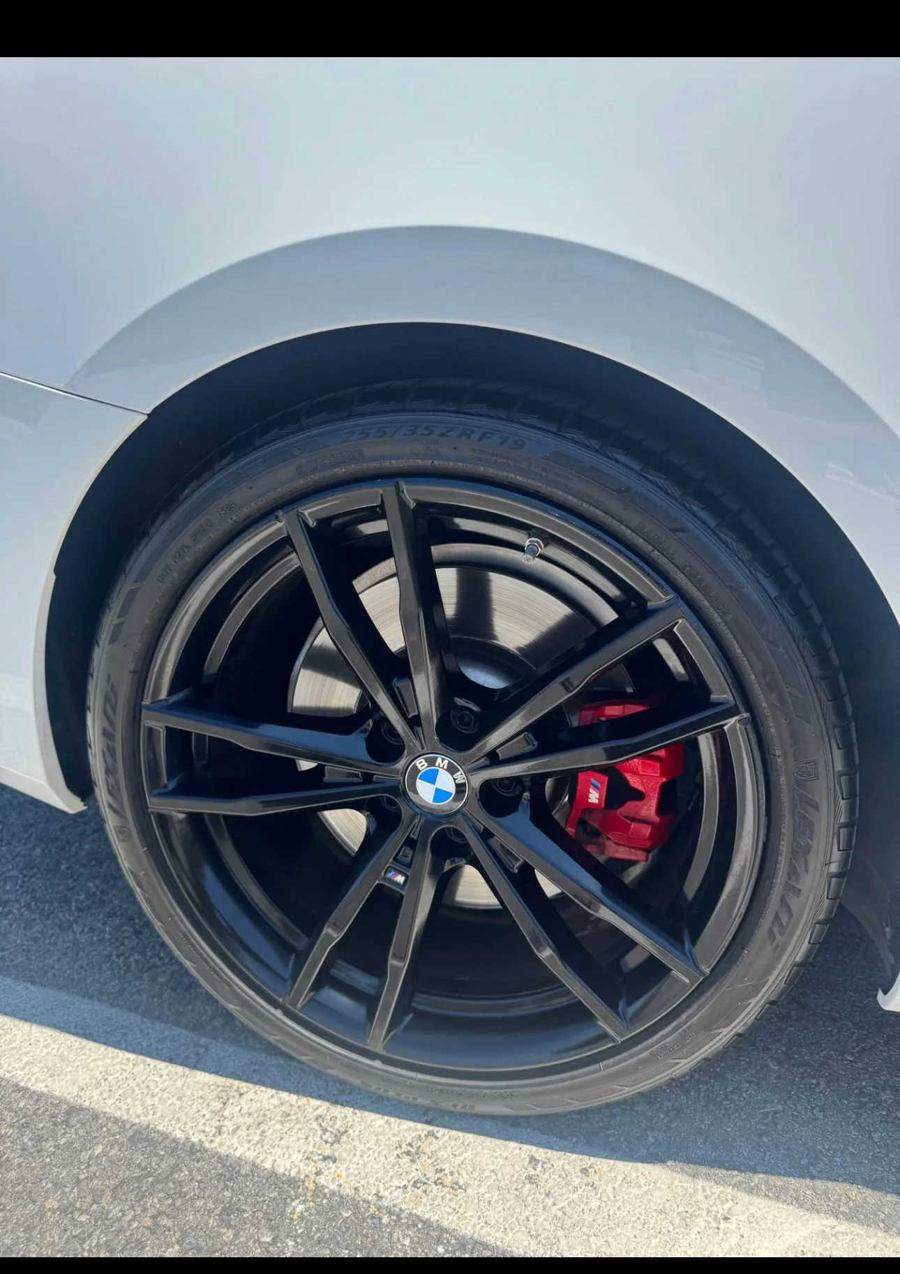 Close-up of a BMW car wheel with a black alloy rim, BMW logo center cap, red brake caliper, and tire with visible size and model markings.