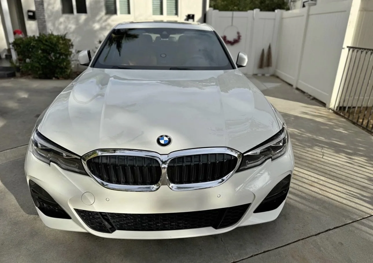 Front view of a white BMW car parked on a driveway in front of a white fence and house.
