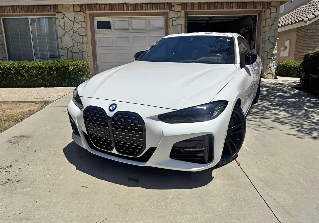 A white BMW car parked on a driveway in front of a house with stone facade, black wheels, and a distinctive grille.