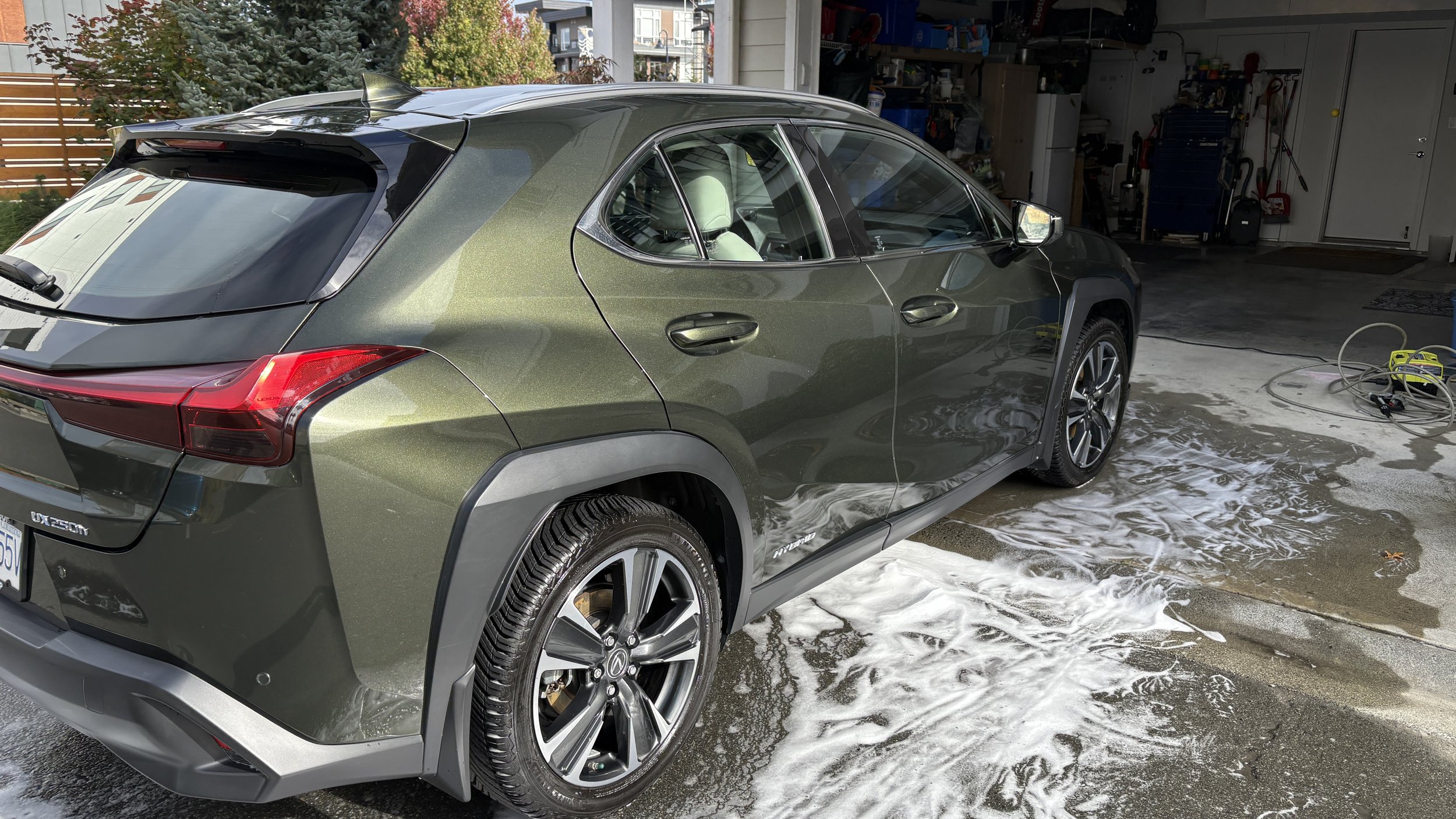 A green Lexus UX 250h vehicle being washed inside a garage with soap suds on the ground.