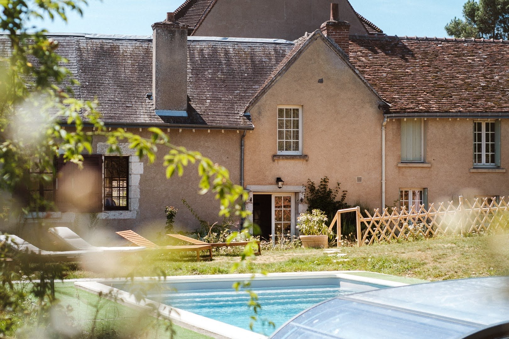 Maison traditionnelle avec piscine, chaises longues et jardin clos.