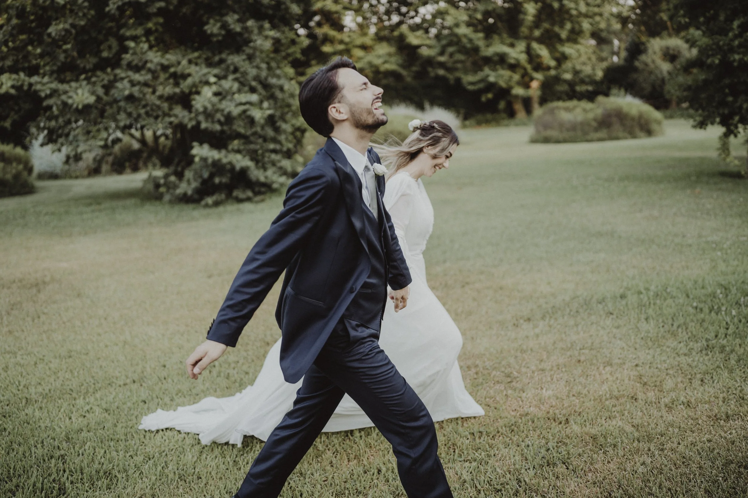Sposo e sposa che camminano nel prato, ridendo e divertendosi durante il matrimonio