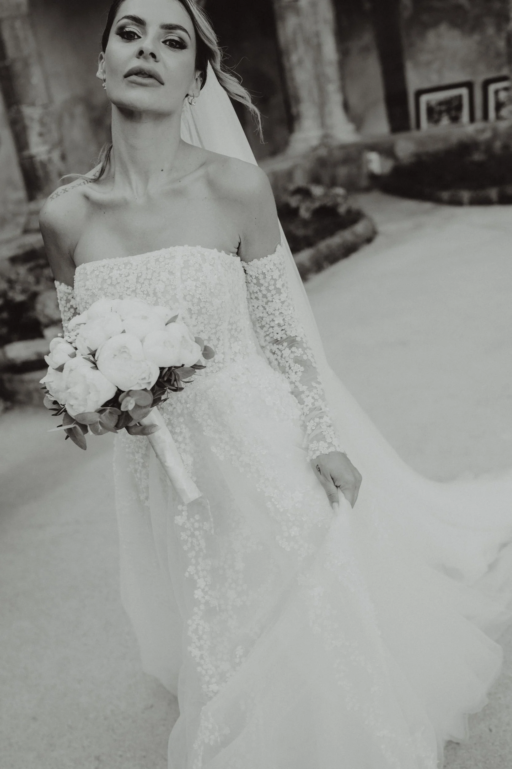 Una donna in abito da sposa tiene un bouquet di fiori bianchi in una foto in bianco e nero.