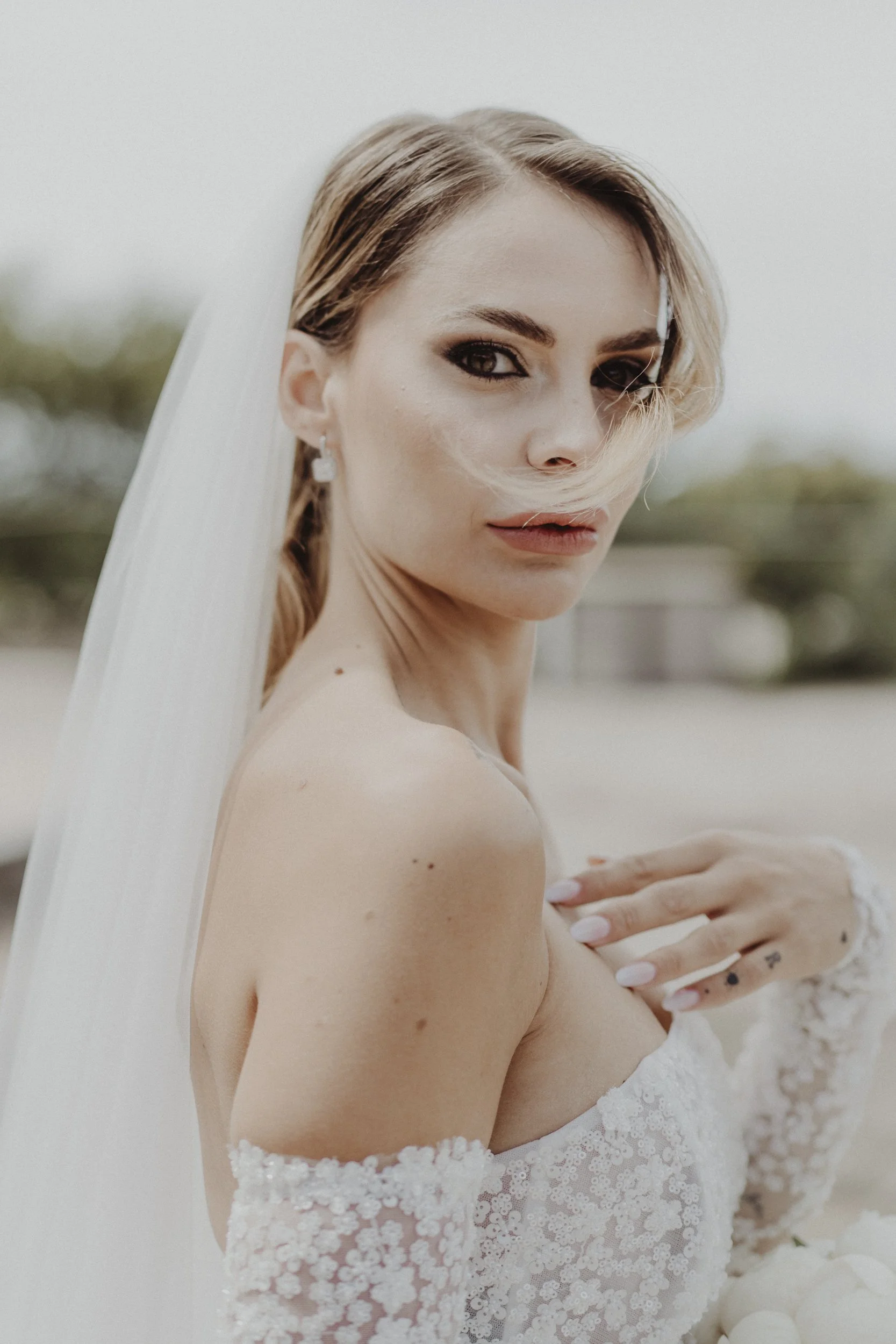 Ritratto di una donna in abito da sposa con dettaglio di pizzo, che guarda verso l'obiettivo con uno sguardo intenso, con capelli sciolti e un velo bianco.