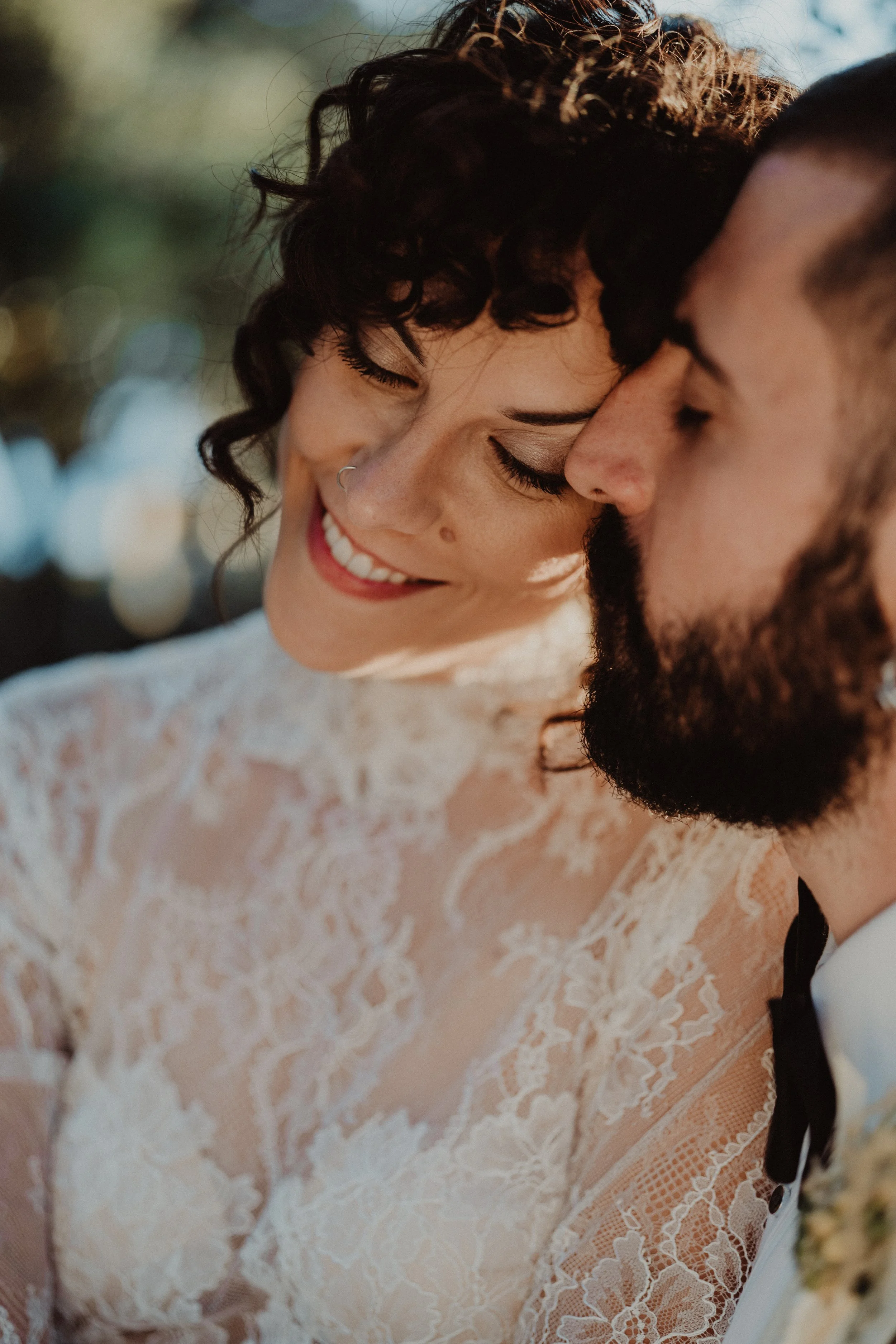 Una coppia di sposi che si abbracciano e sorridono, con dettagli in pizzo sulla loro abbigliamento da matrimonio