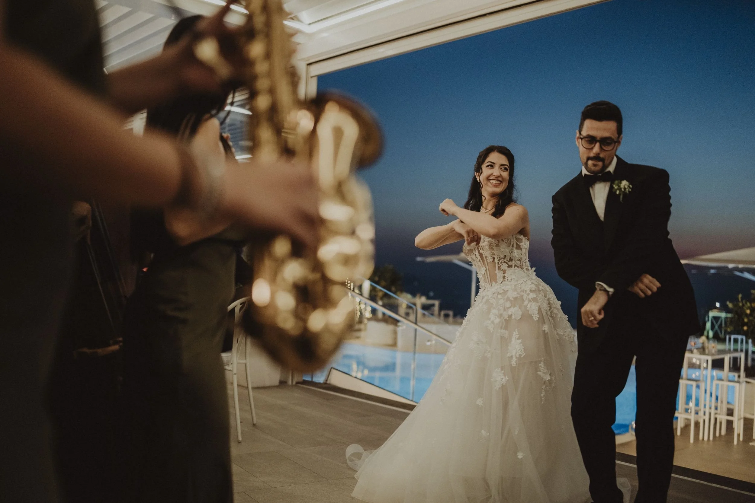 Una coppia di sposi di fronte a un'orchestra, durante un matrimonio serale con una vista sul mare, al tramonto.