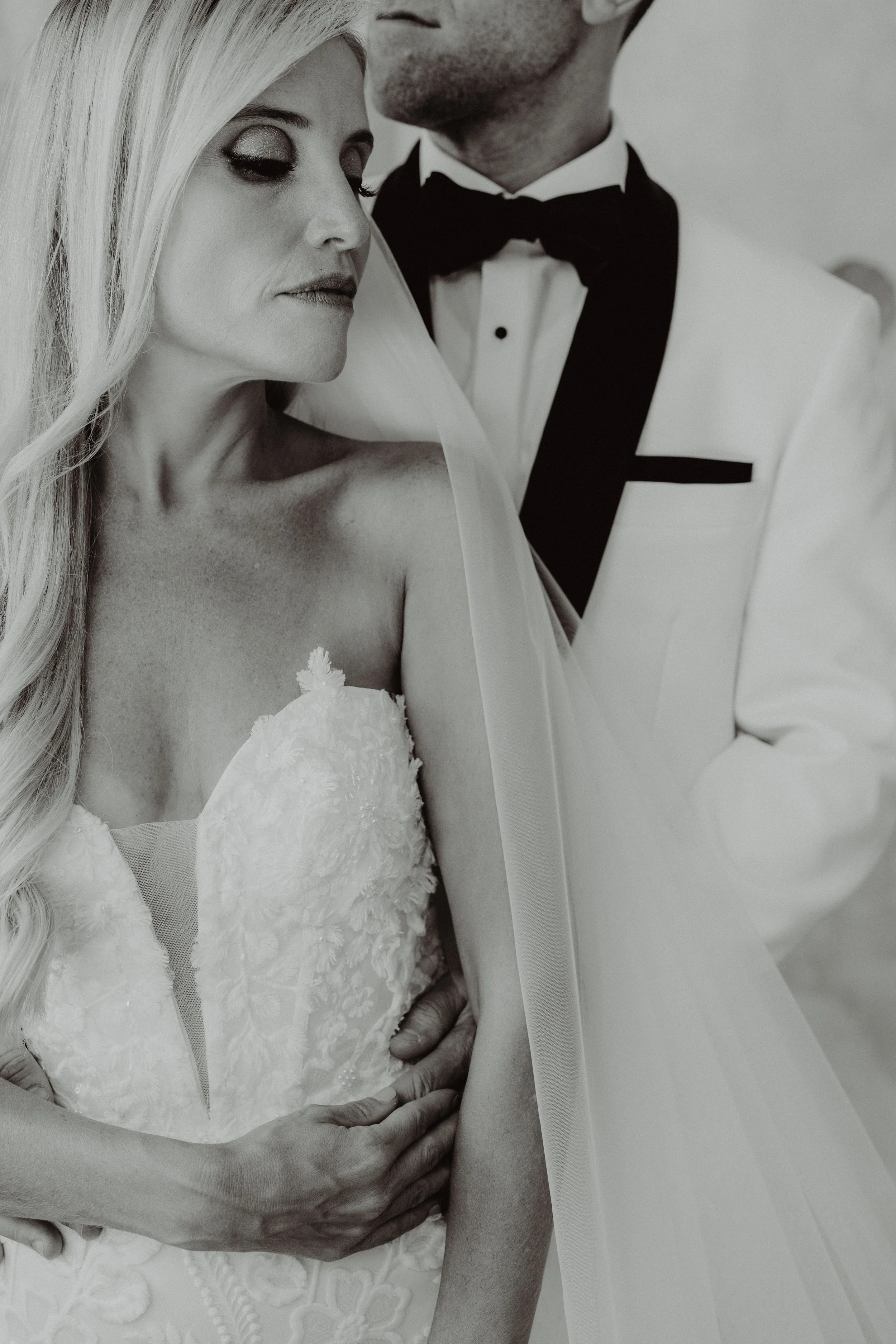Una coppia in abito da sposa e completo da matrimonio, si abbraccia in un'istantanea di matrimonio in bianco e nero.