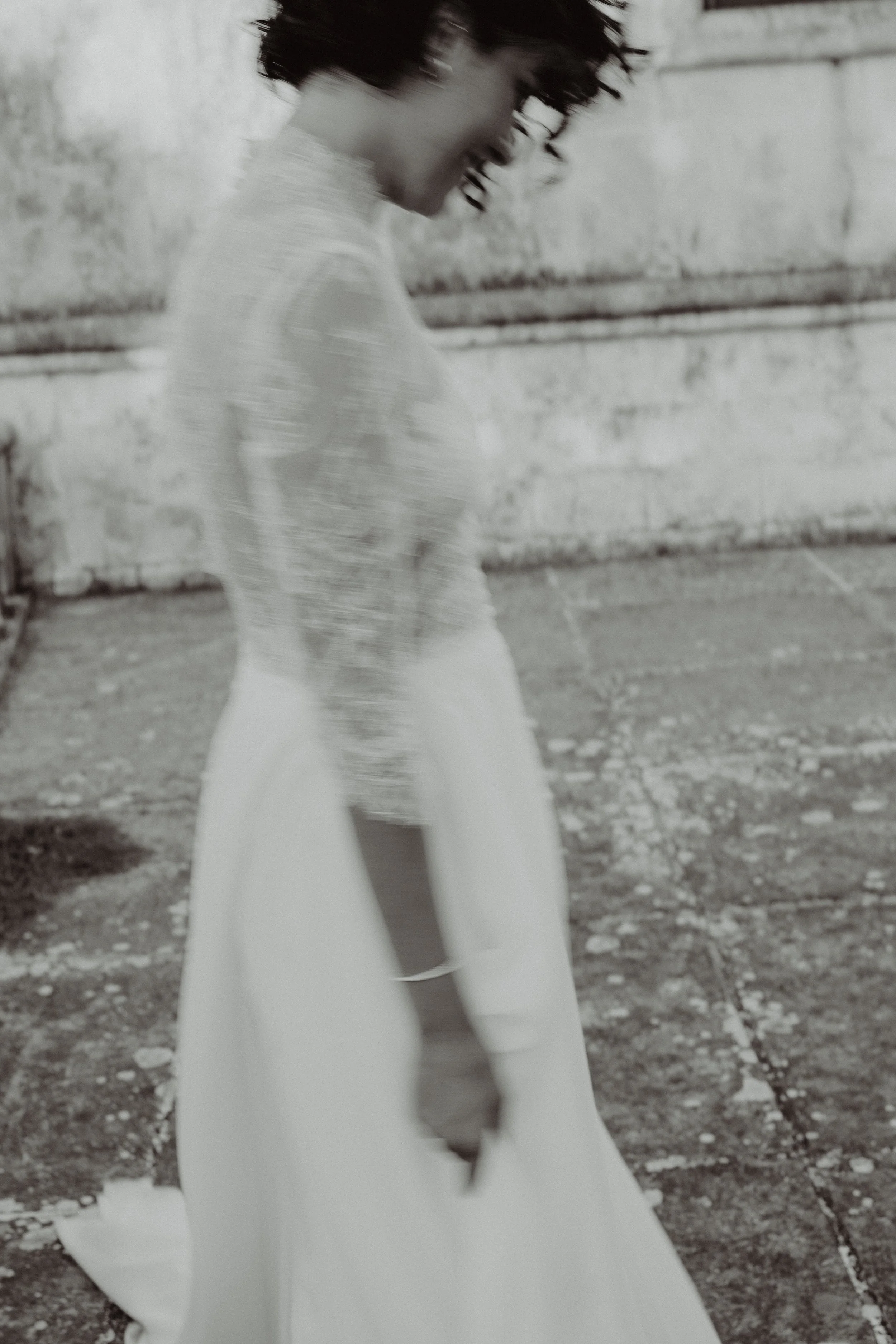 Una donna con abito bianco, capelli ricci, in piedi su una strada di cemento, rivolta verso il basso.