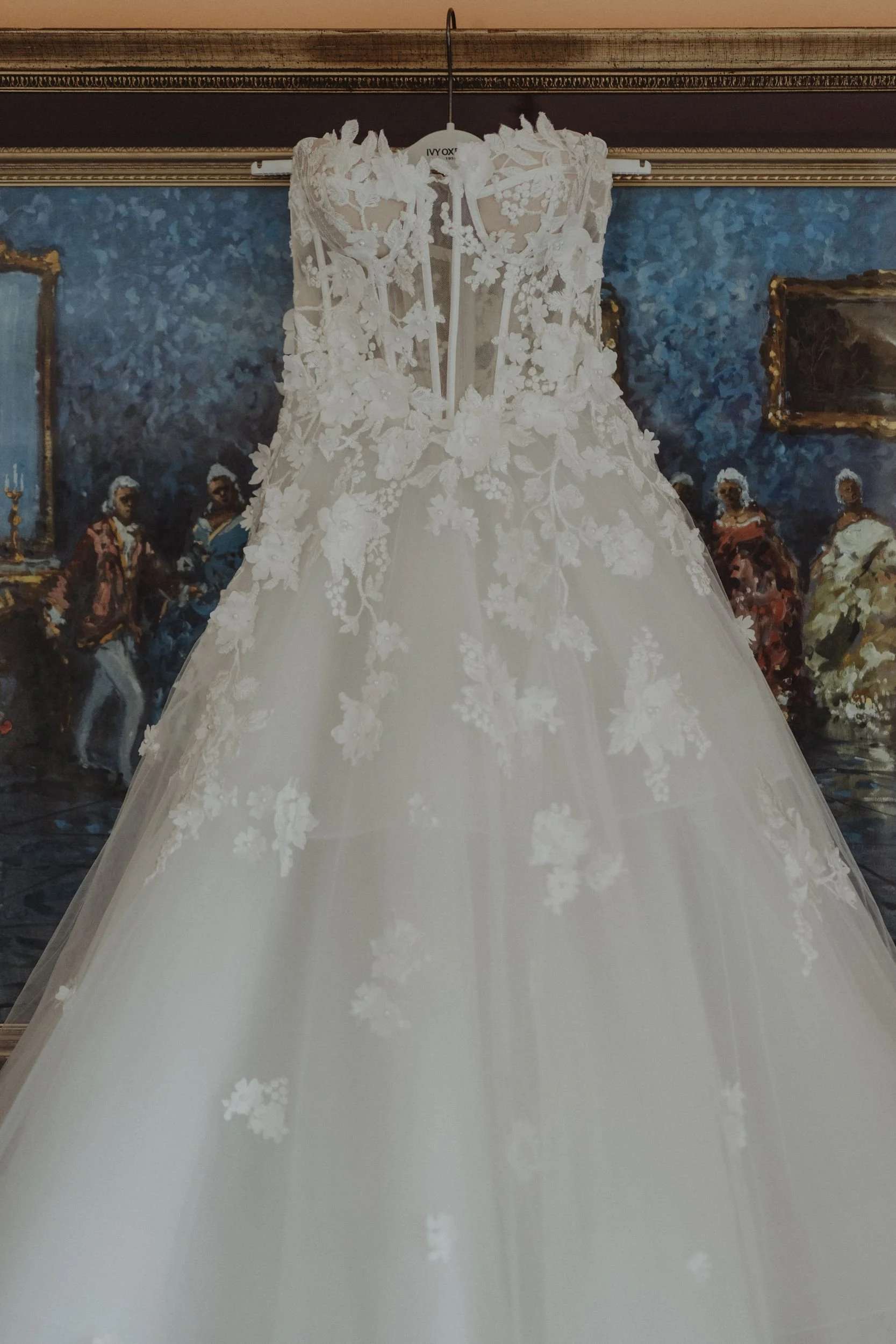 Abito da sposa bianco con dettagli in lace e applicazioni floreali, appeso a una gruccia.