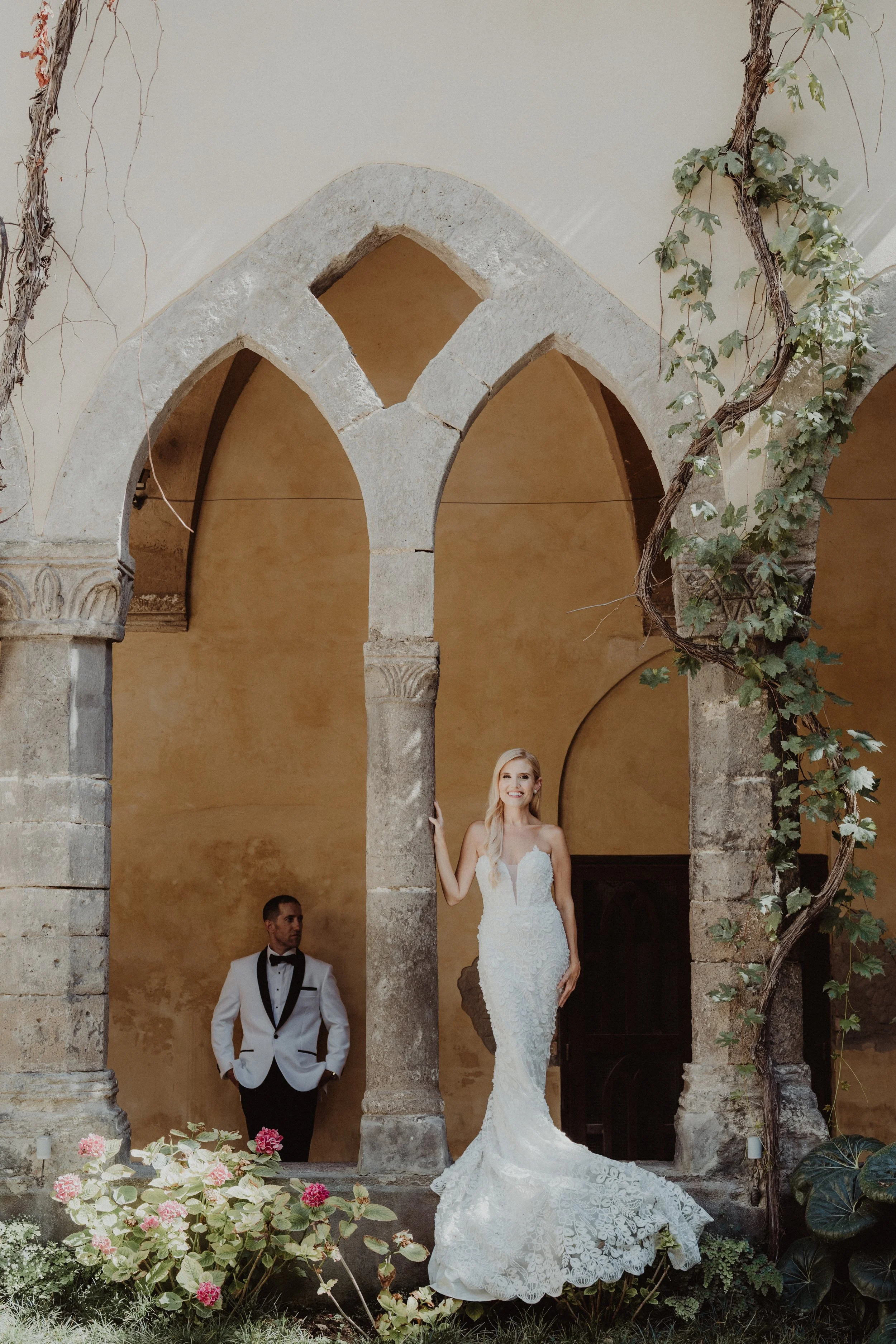 Sposa con abito da matrimonio bianco in una location storica con arcate in pietra e piante