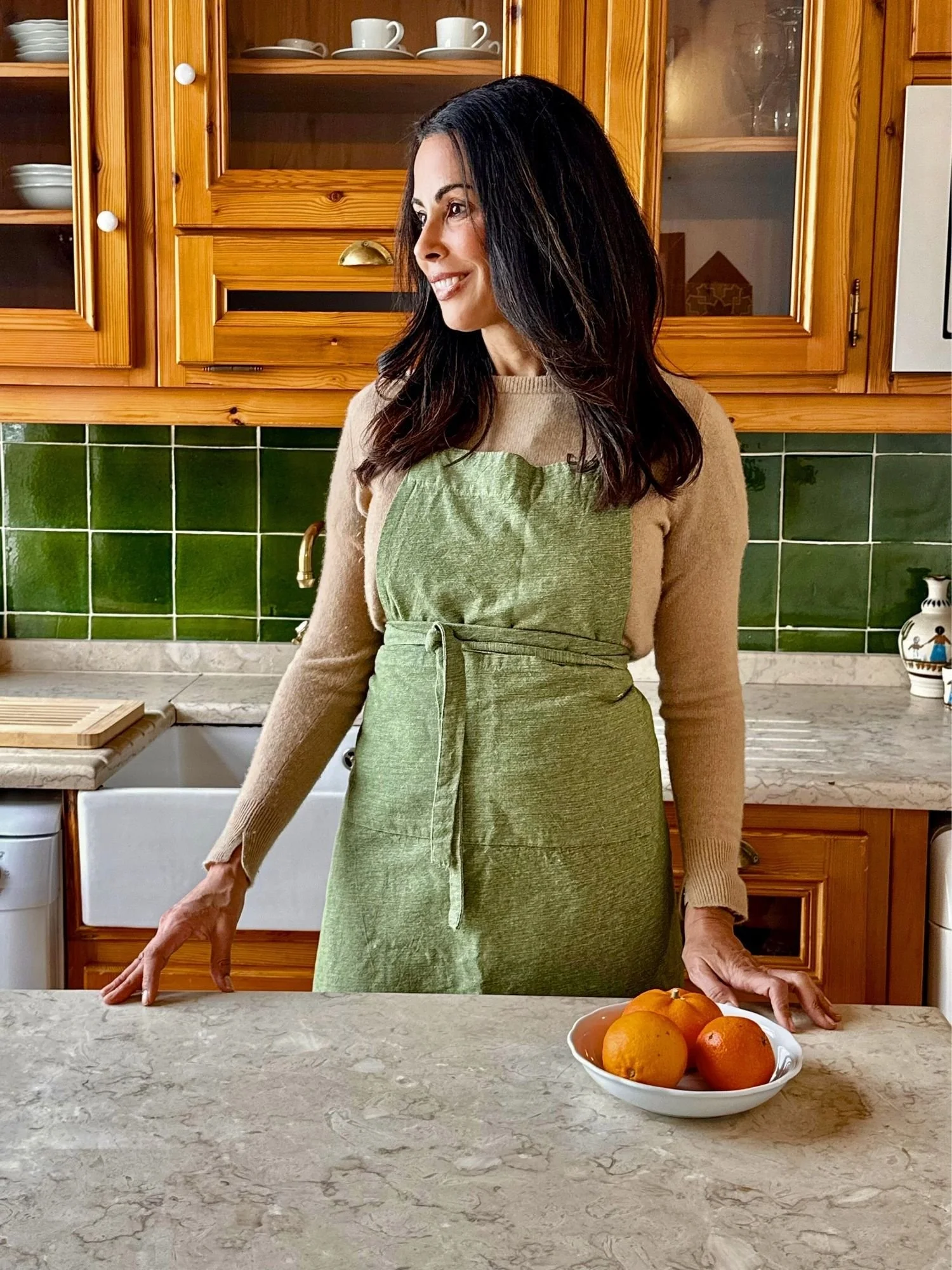Content strategist and copywriter, Melissa Renée Maxwell standing and smiling in a kitchen looking to the left in a green apron with green tile.