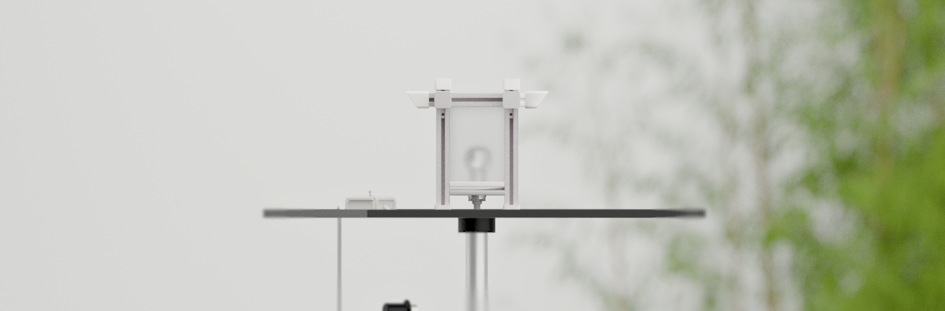 A modern lamp on a stand with a black horizontal bar, white vertical supports, and a small box attached to the left side, set against a blurred background of bamboo shoots and sky.
