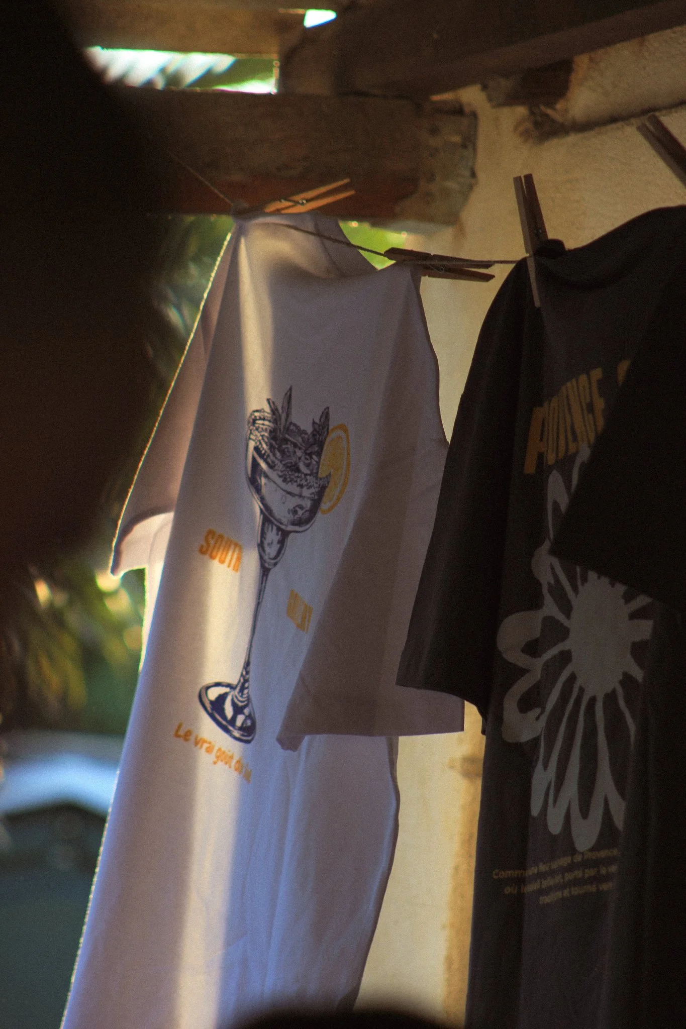 Un t-shirt blanc SouthGallery est suspendu à une corde à linge à l'aide de pinces en bois.