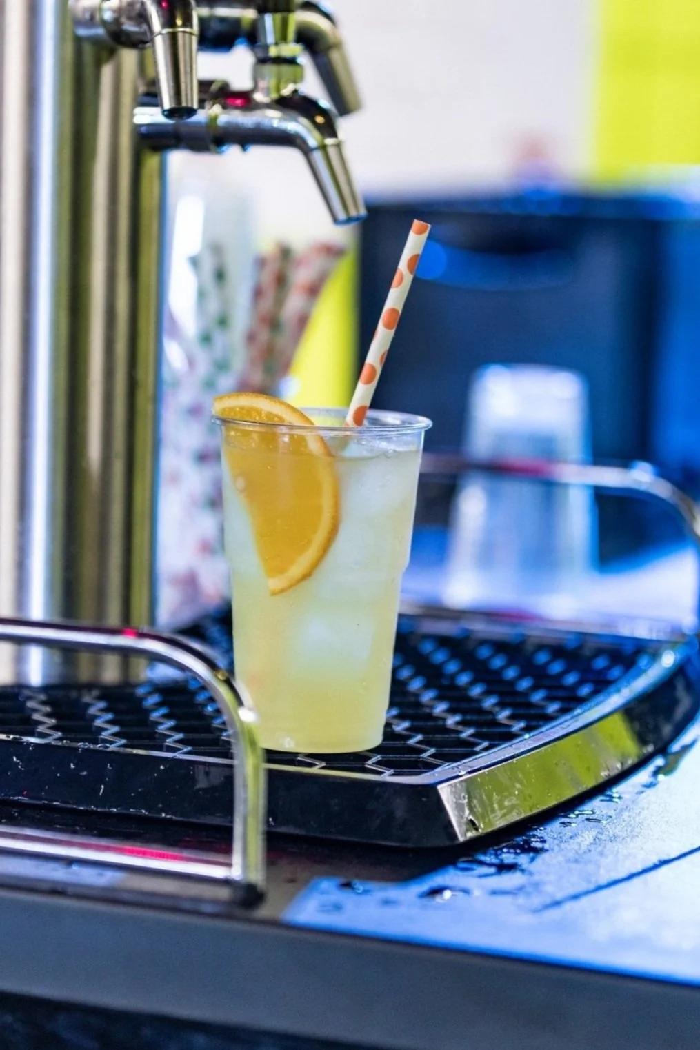 A glass of lemonade with a slice of lemon and a striped straw, placed under a soda fountain tap.
