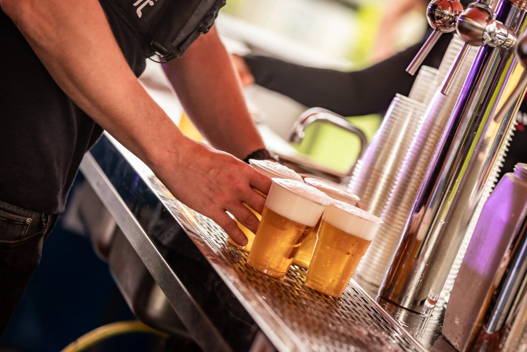 A person placing glasses of beer under a tap at a bar or brewery.