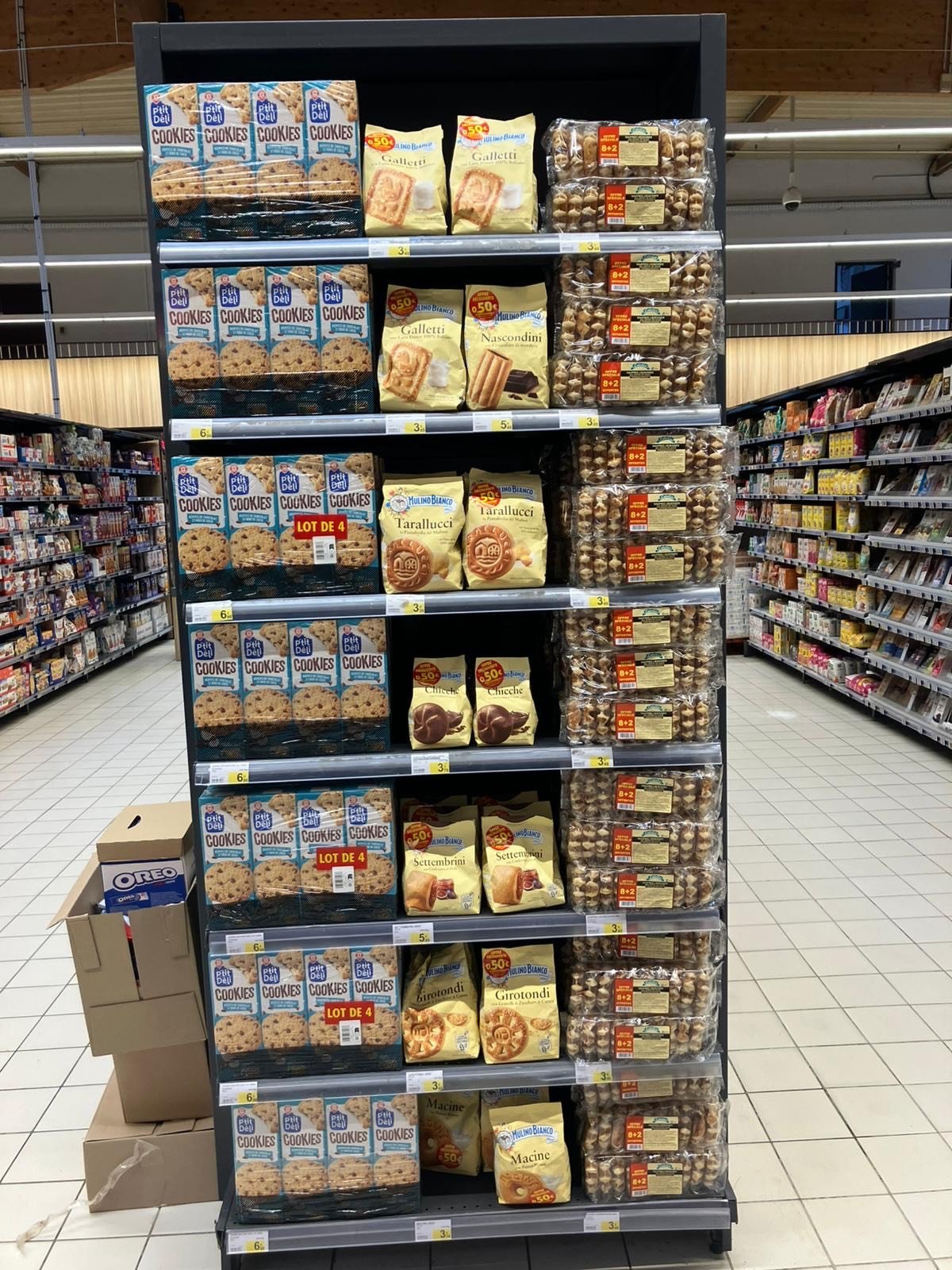 Une étagère de supermarché remplie de différentes marques de biscuits et gâteaux, avec des paquets de cookies, Galleti, Nascondini, Tarallucci, Settembrini, Girotondi, et Macine, et des sacs de gâteaux, dans une allée de magasin.