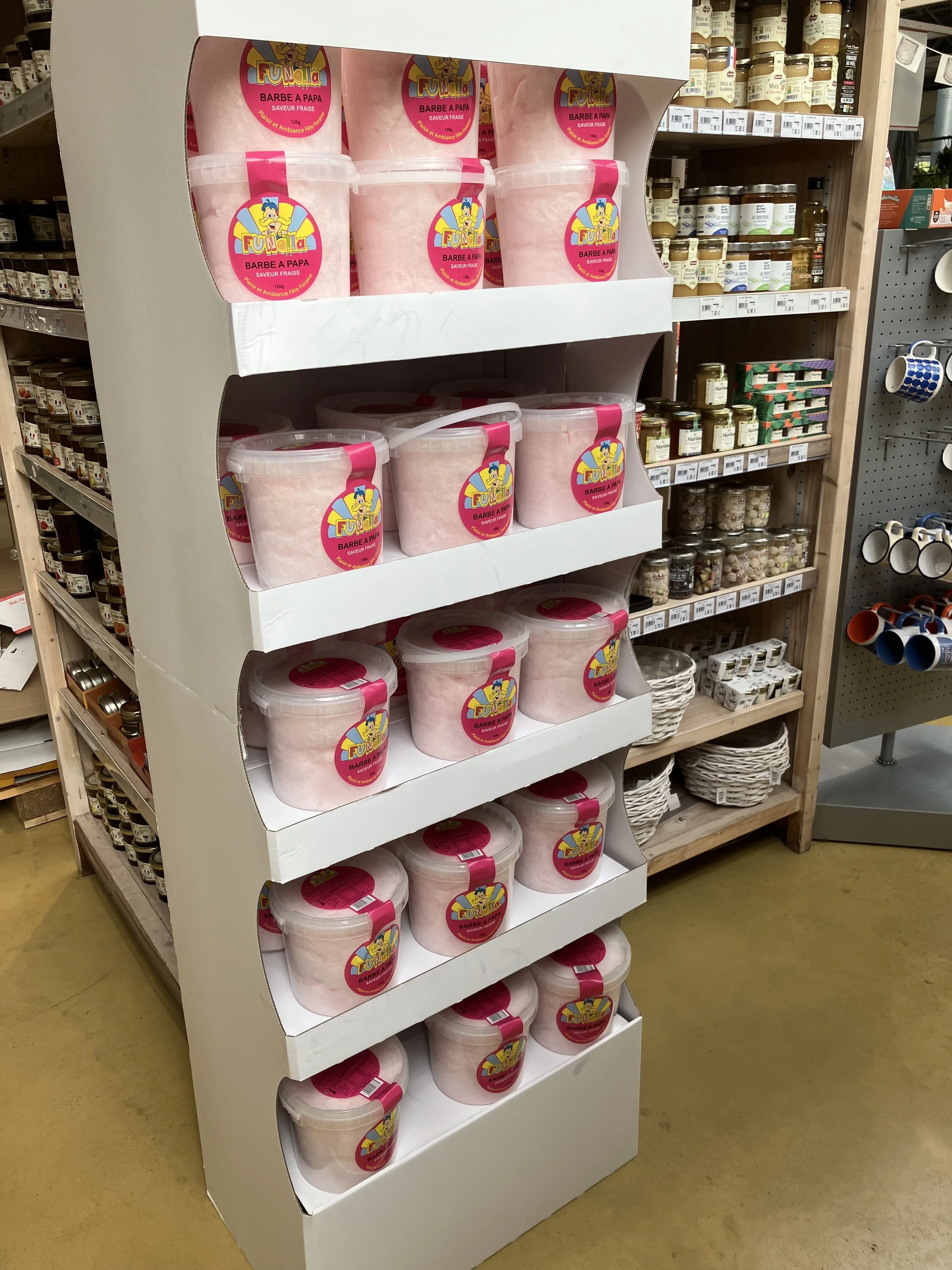 Présentoir avec plusieurs pots de barbe à papa à la fraise dans un magasin.