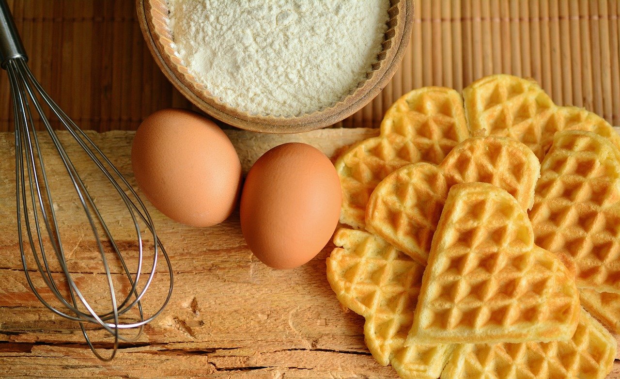 Gaufres, œufs, farine et un fouet sur une surface en bois.