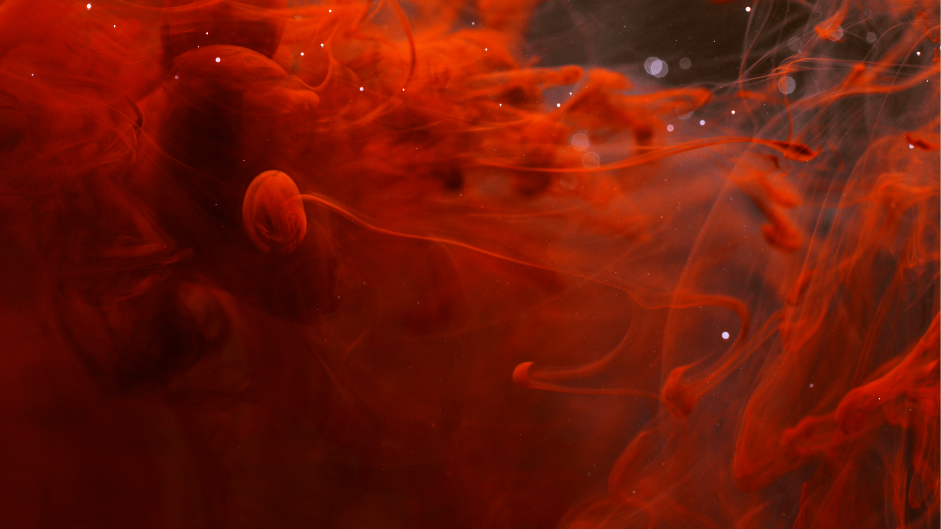 Abstract image of swirling red and black nebula with small white stars scattered throughout.