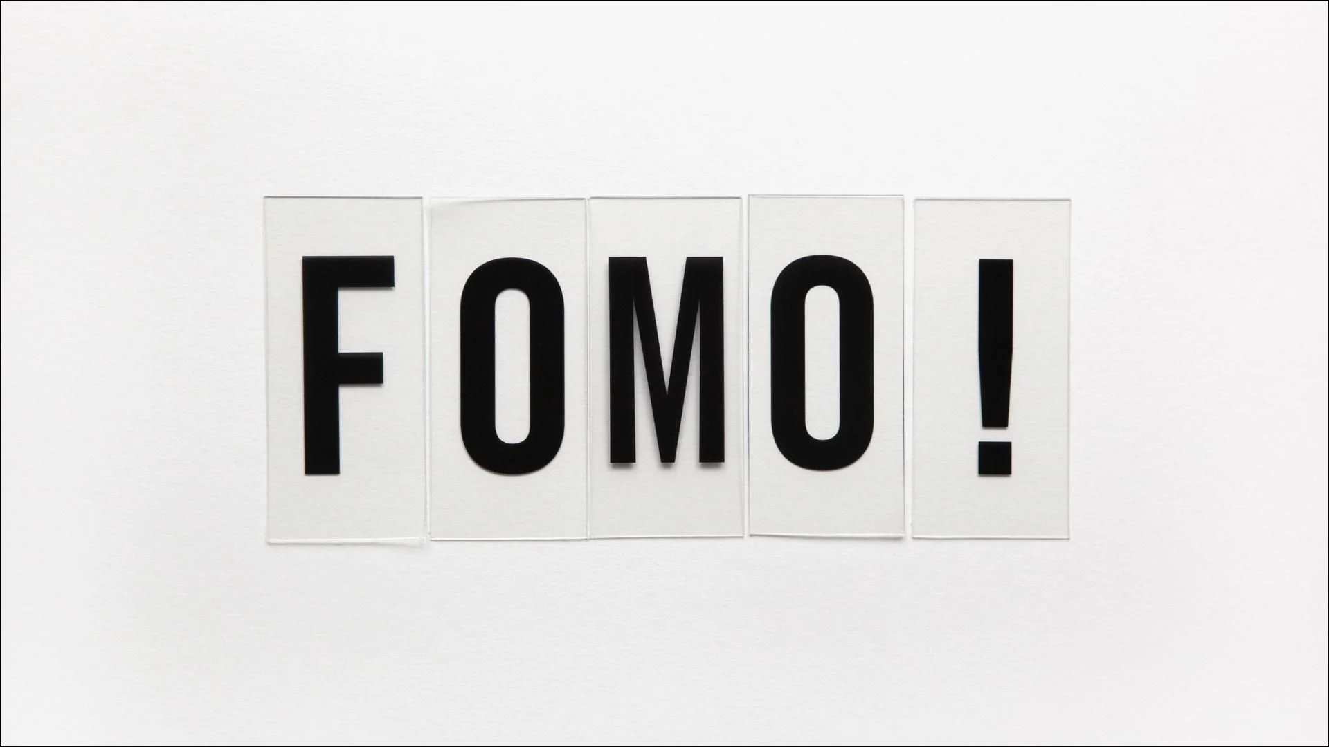 Ein weißer Hintergrund mit vier Buchstaben, die das Wort „FOMO“ bilden, und ein Ausrufezeichen