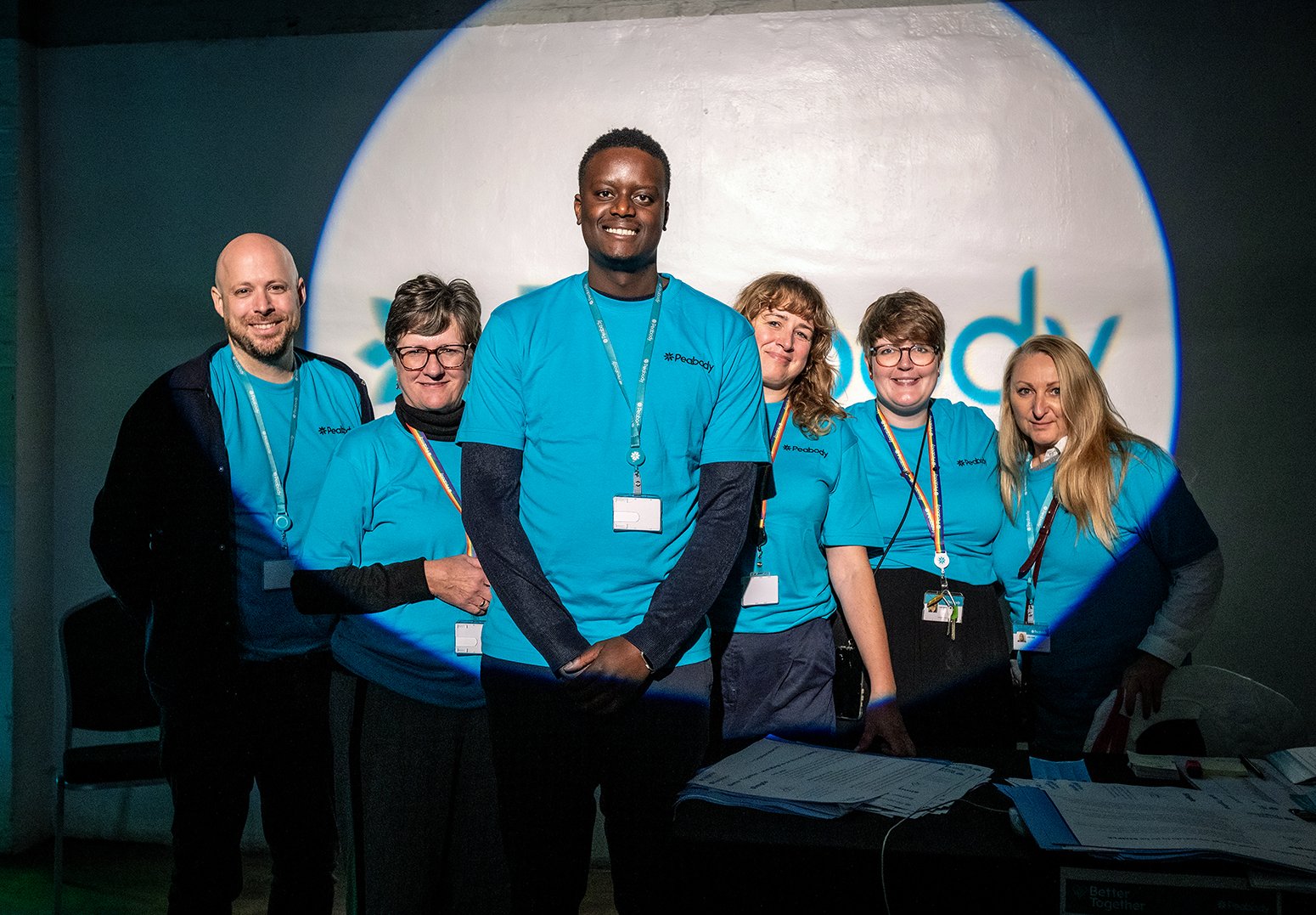 Photograph of a group of people wearing blue T-shirts standing together in front of a circular illuminated backdrop at an event.
