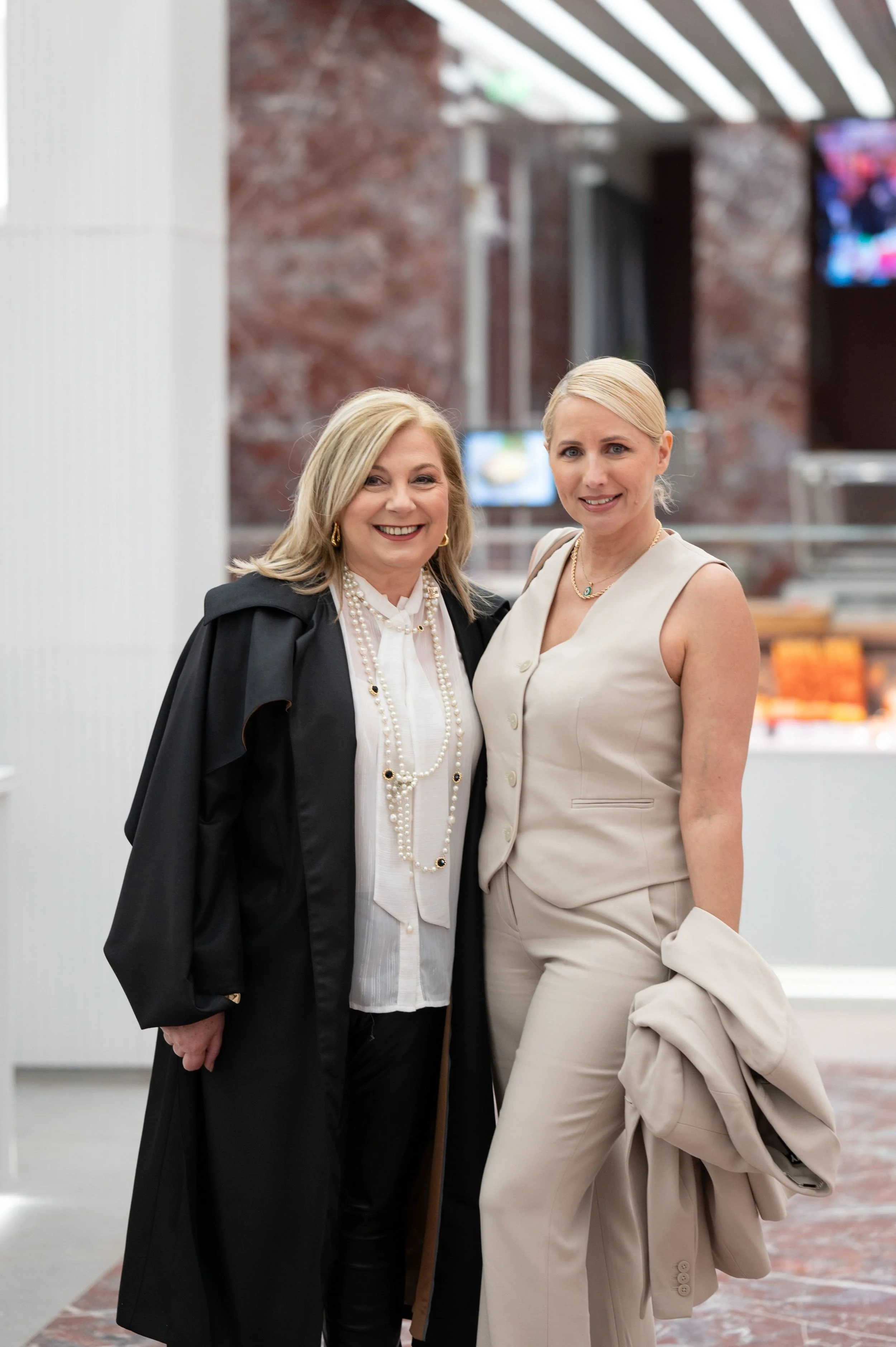 Two women posing together at a corporate event in a bright indoor venue