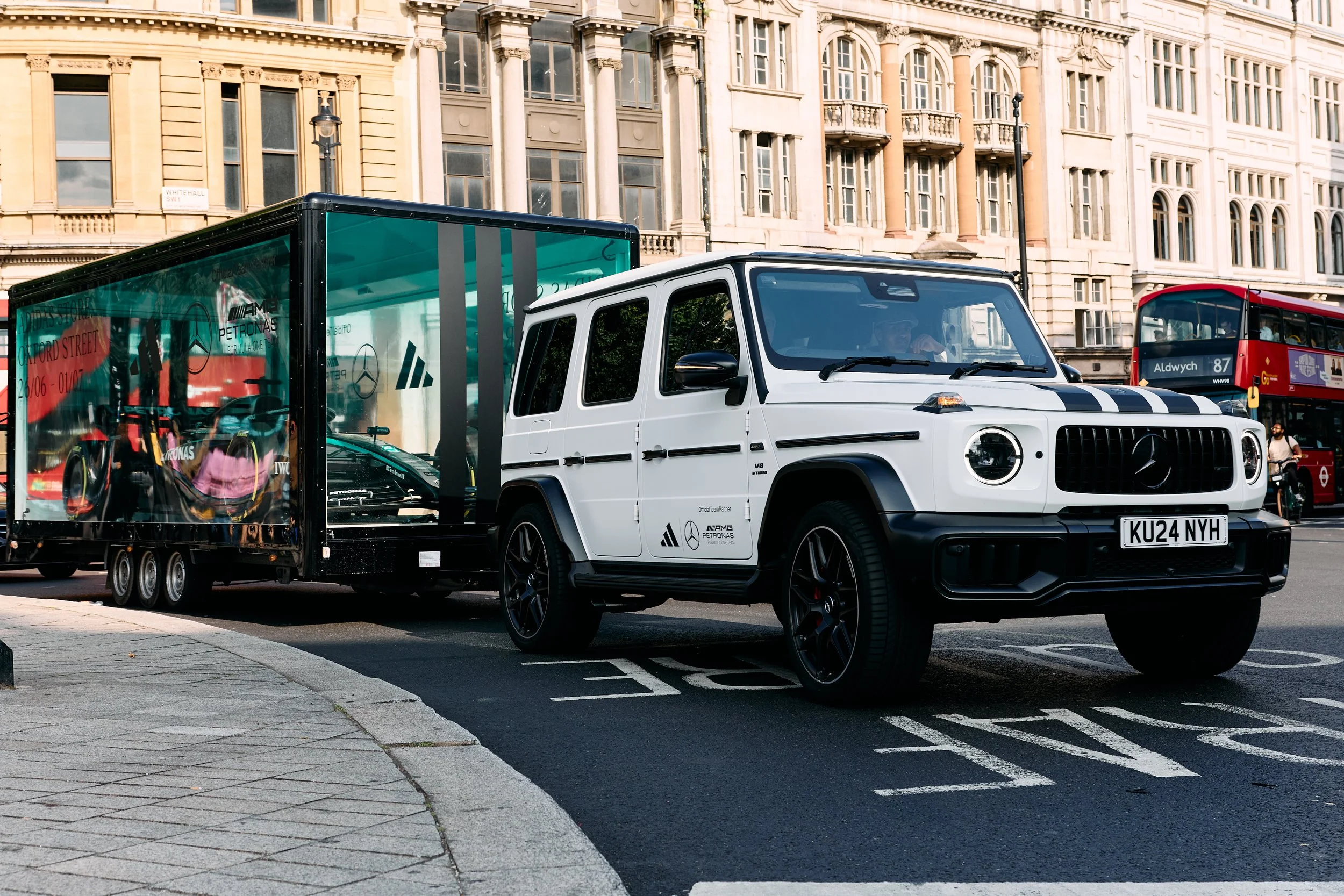 Mercedes G-Class towing Formula 1 race car in glass trailer through London street, promotional AMG Petronas display