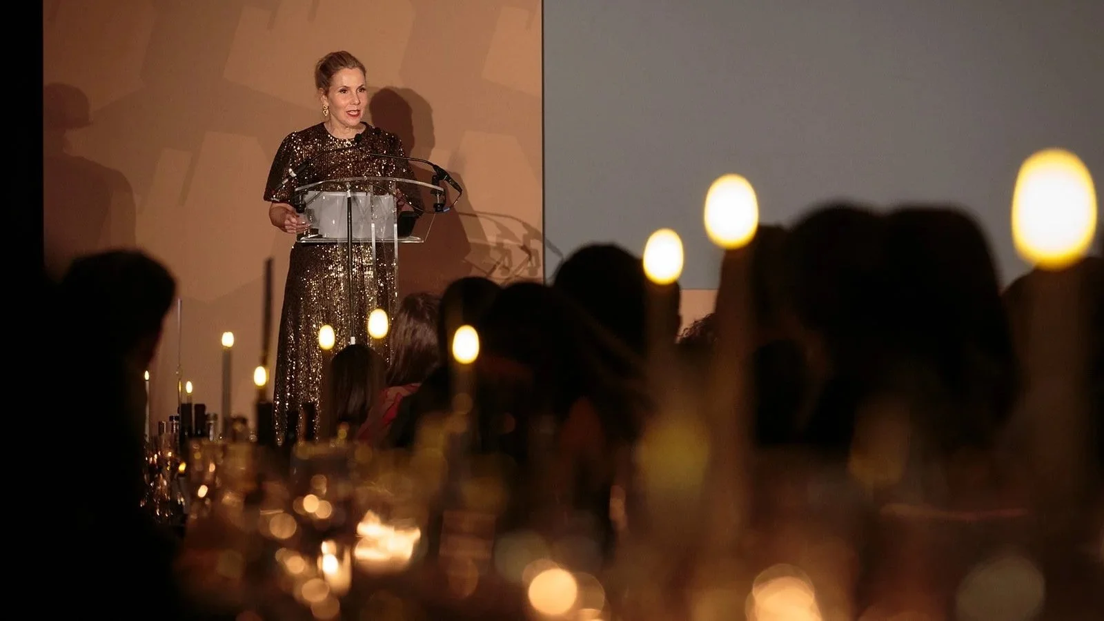 Woman in a sequinned dress speaking at a clear lectern during the Effie Awards in London, with seated guests in the foreground.