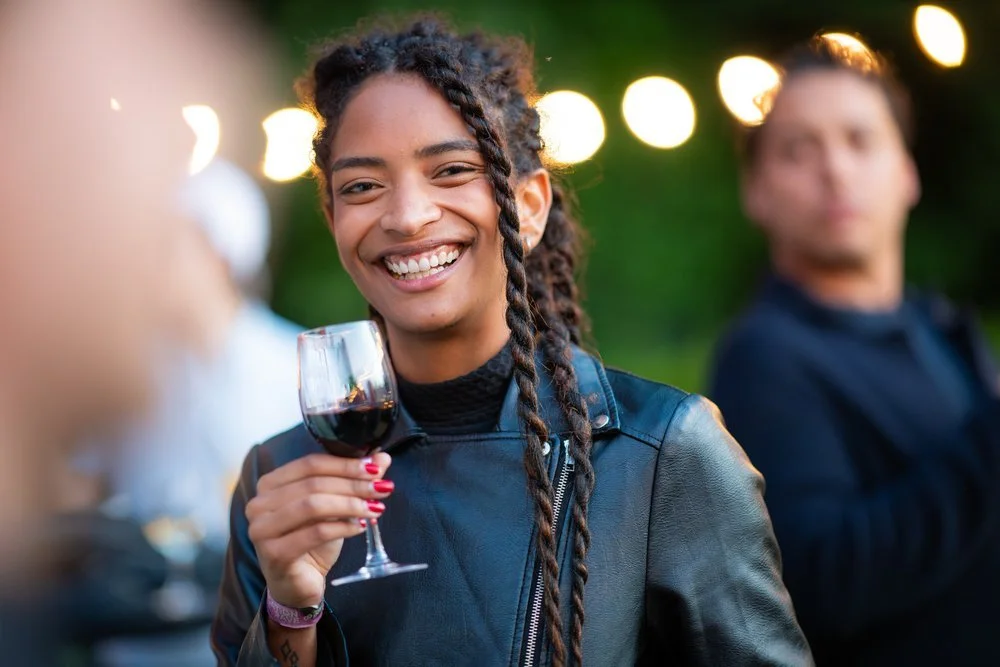 Guest holding a glass of red wine and smiling during an outdoor networking event.