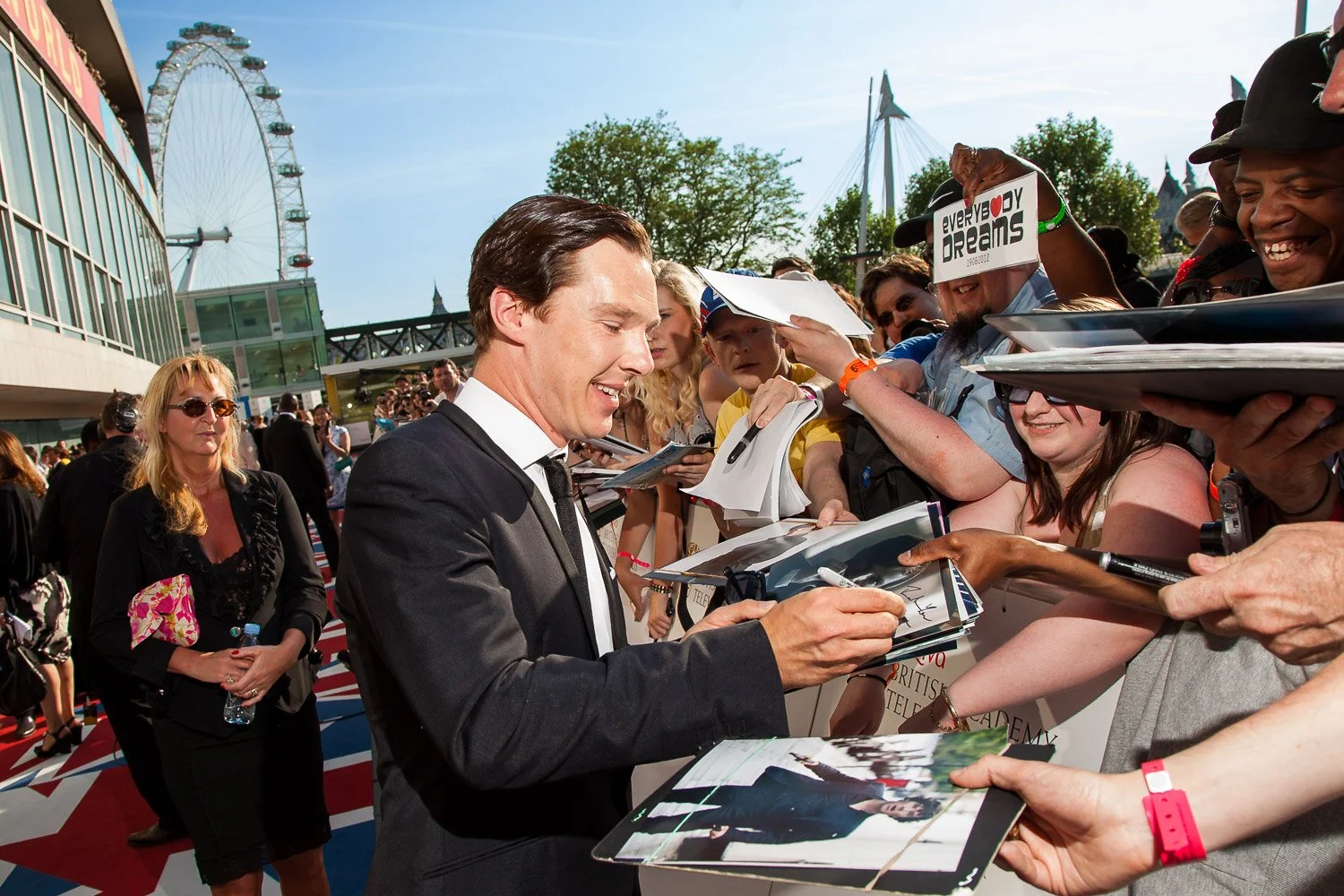 Guest signing autographs for fans during a red-carpet event outside a London venue.
