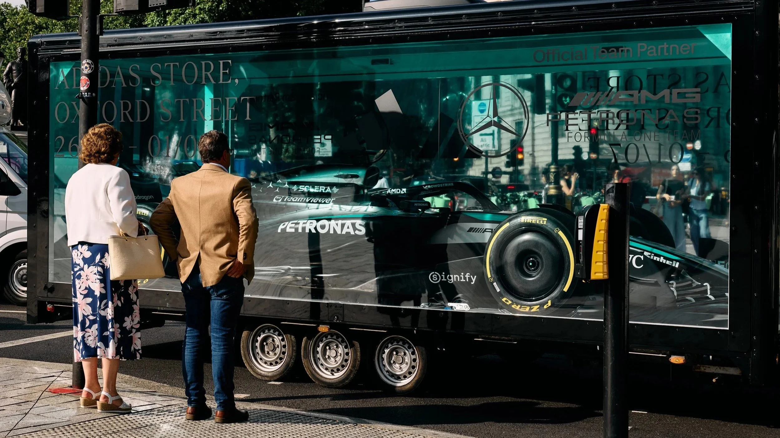 Two people viewing a Mercedes Formula 1 car in a glass-sided trailer at the Adidas x Mercedes motorsport activation in London.
