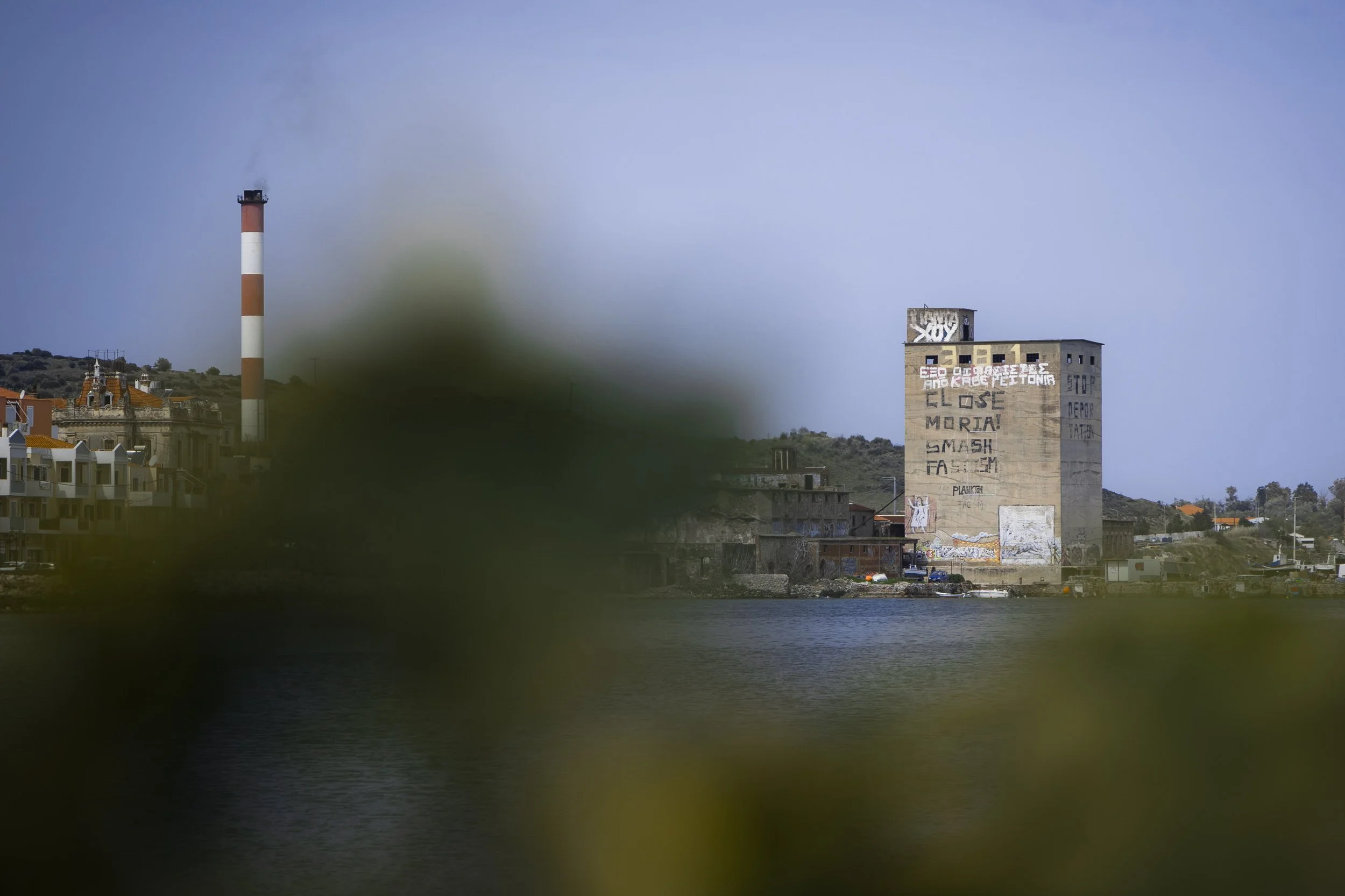 Remnants of memories from previous years scattered across the island: on the left, a building next to one of Mytilene's bays; on the right, the trailer of a humanitarian aid truck, abandoned next to various watercrafts.