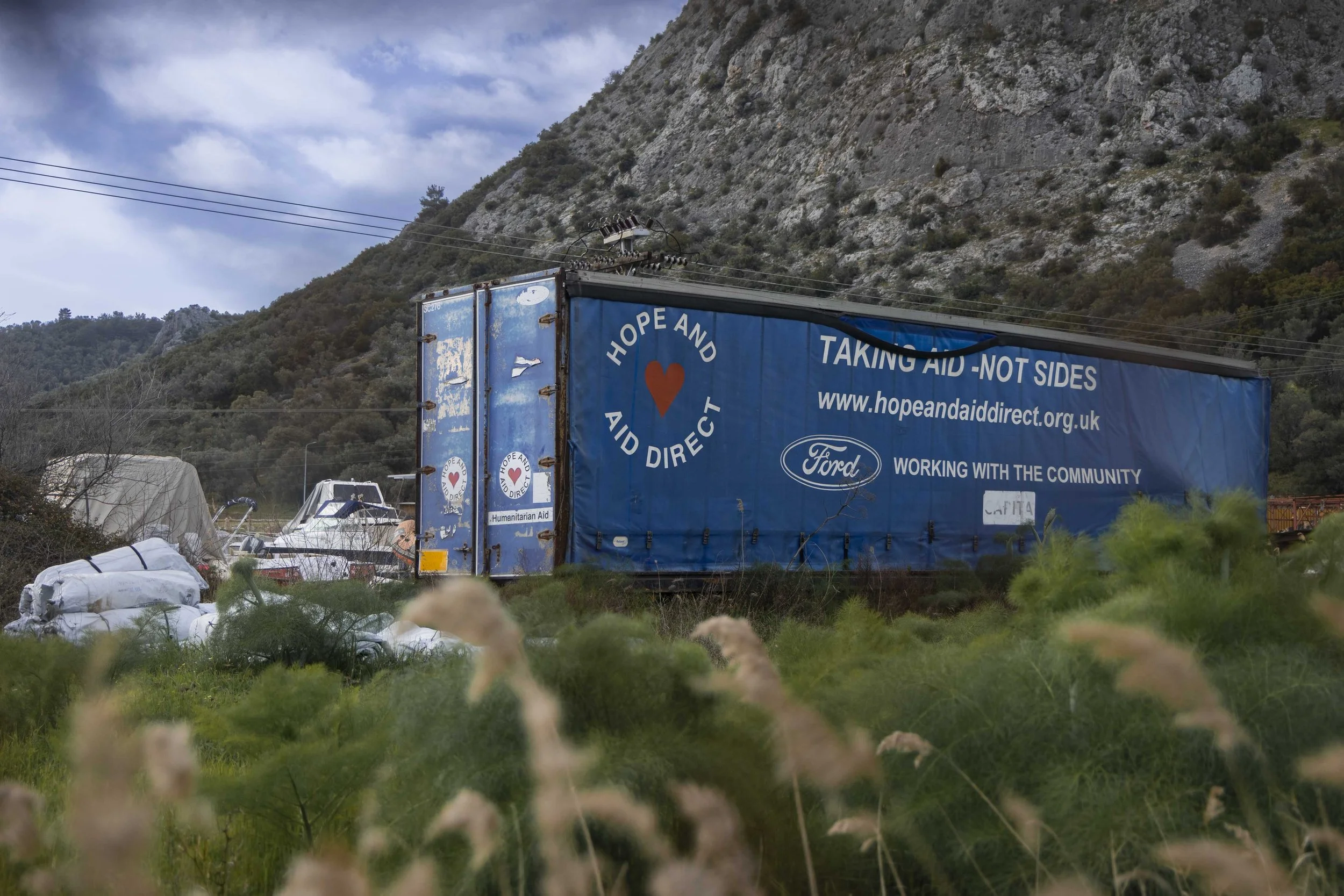 Remnants of memories from previous years scattered across the island: on the left, a building next to one of Mytilene's bays; on the right, the trailer of a humanitarian aid truck, abandoned next to various watercrafts.